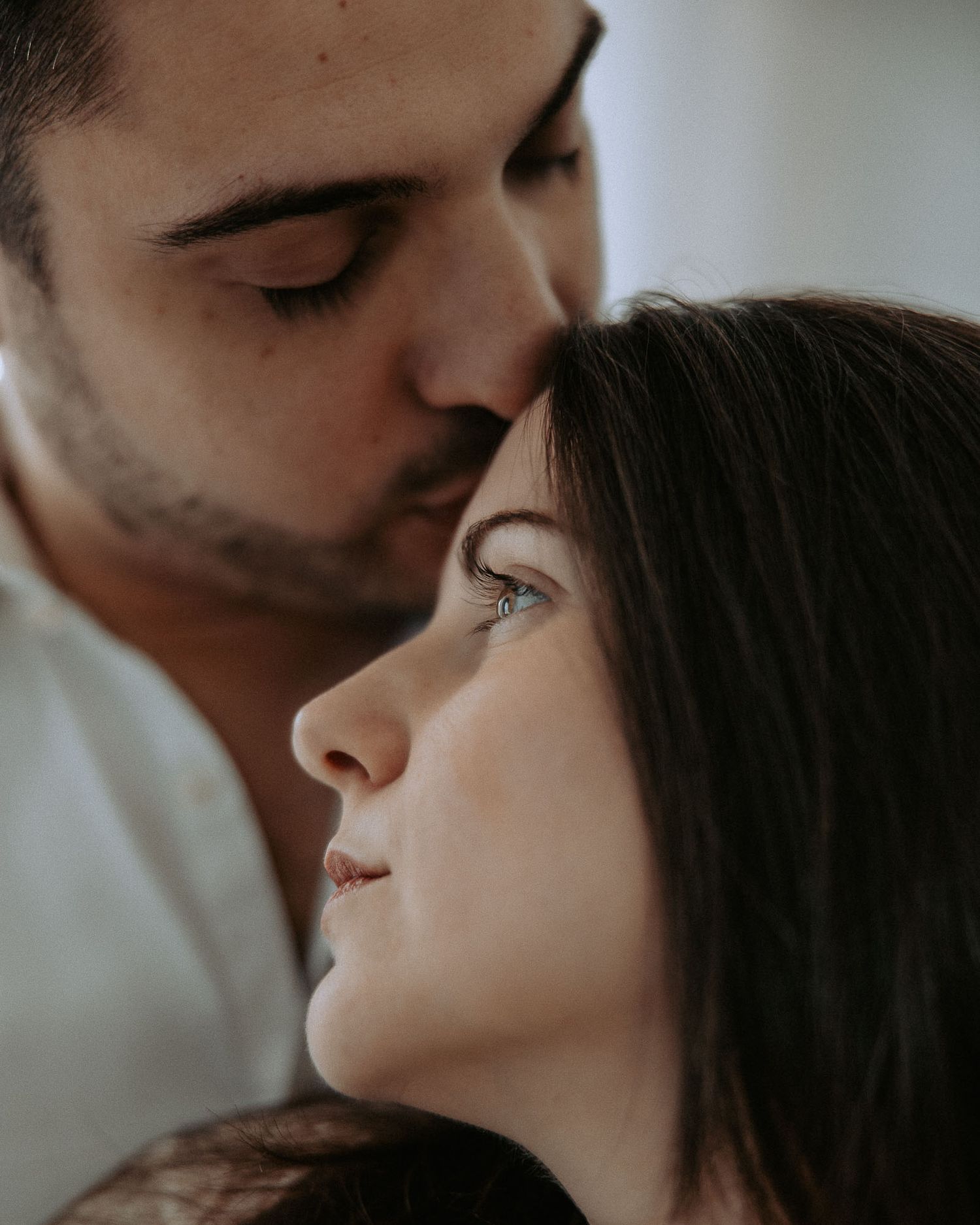 Un uomo bacia teneramente una donna sulla fronte mentre lei guarda lontano, catturando un intimo momento romantico.