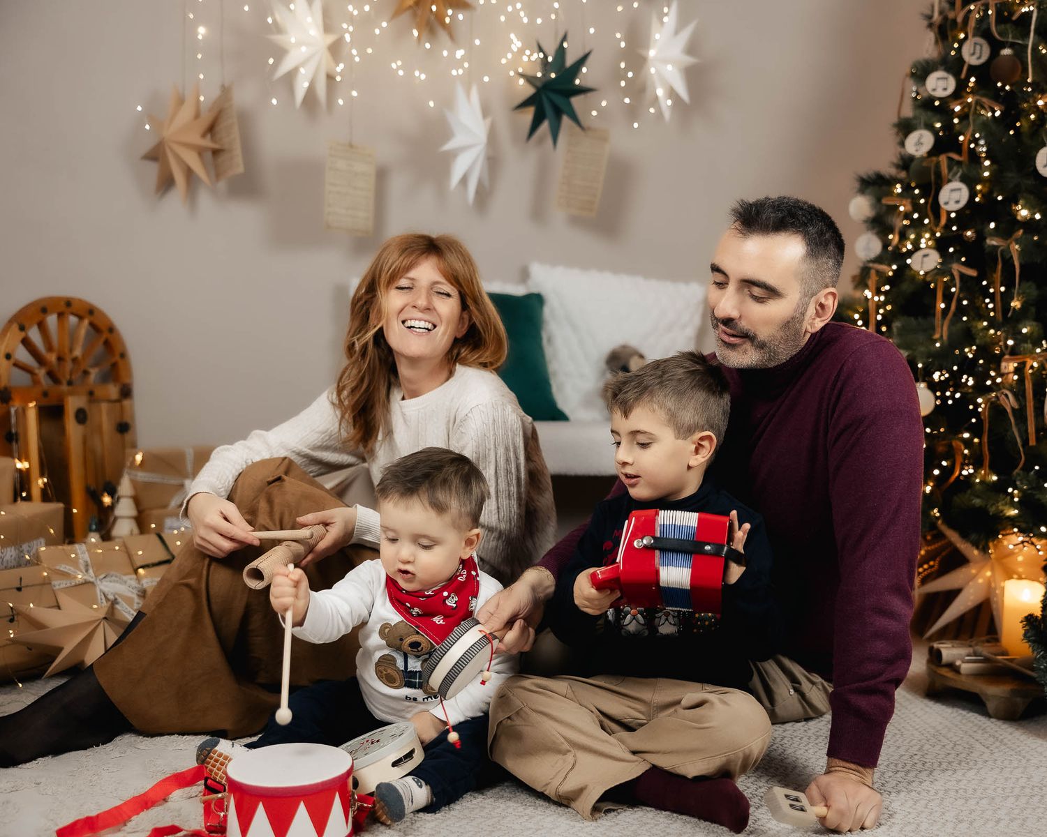 Family of four enjoying Christmas morning with toys, decorations, and a festive tree in a cozy holiday setting.
