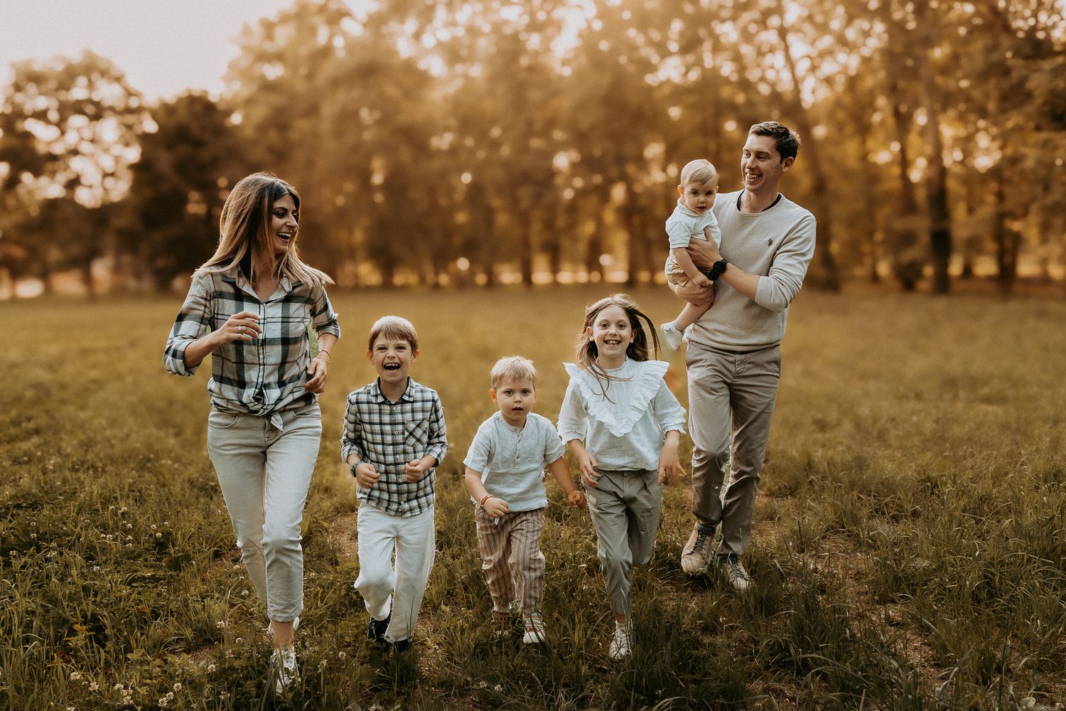 Happy family with four children running and laughing together in a sunny autumn park field.