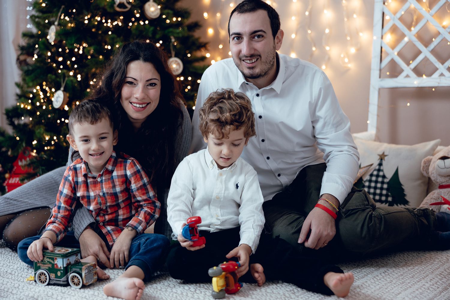 Family enjoying Christmas time together near decorated tree with string lights.