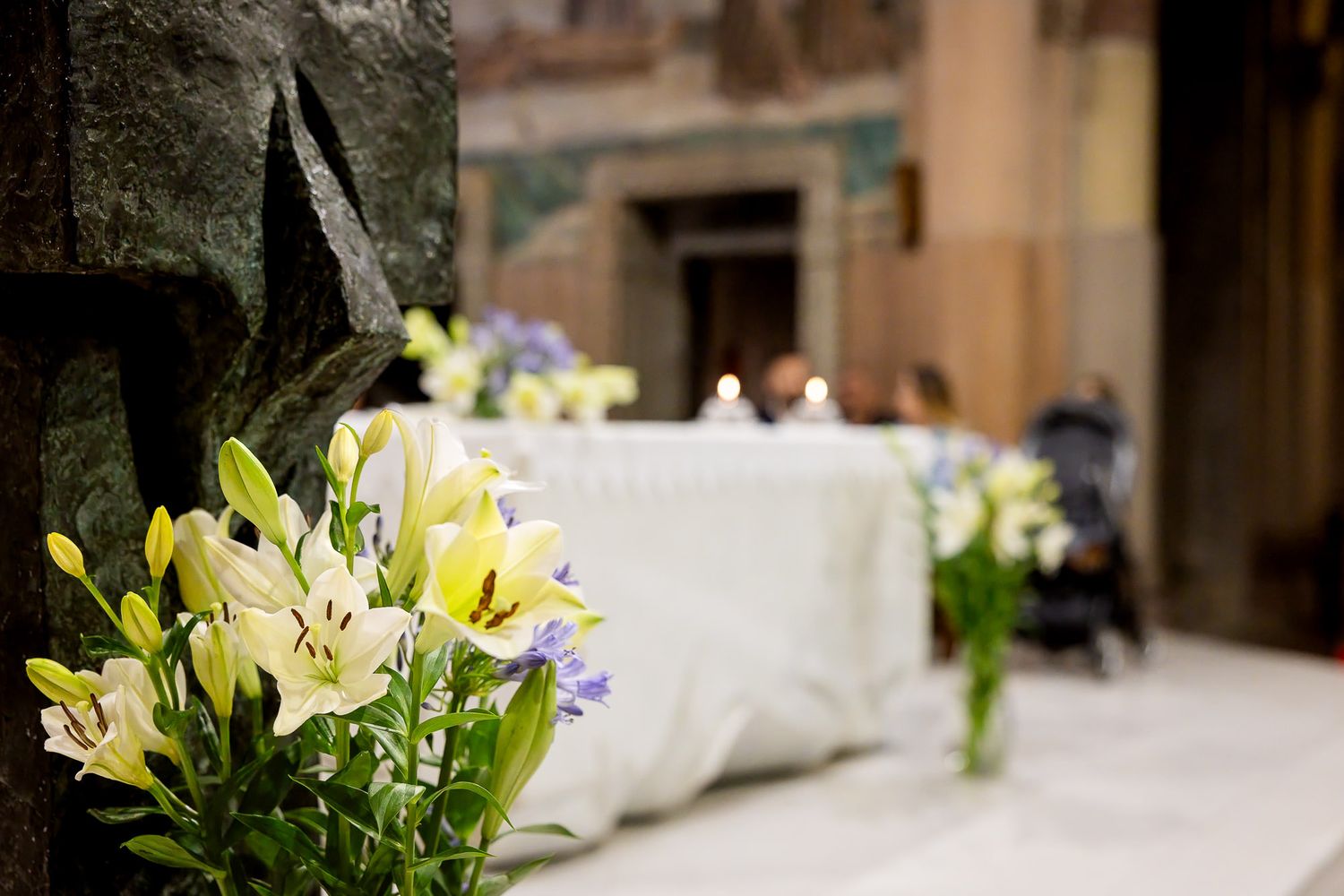White and yellow lilies arranged near a draped altar table in a softly lit church for a baptism ceremony.