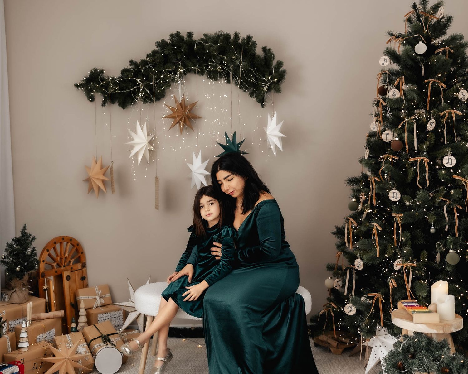Mother and daughter in matching green velvet dresses pose together near a decorated Christmas tree with star ornaments.