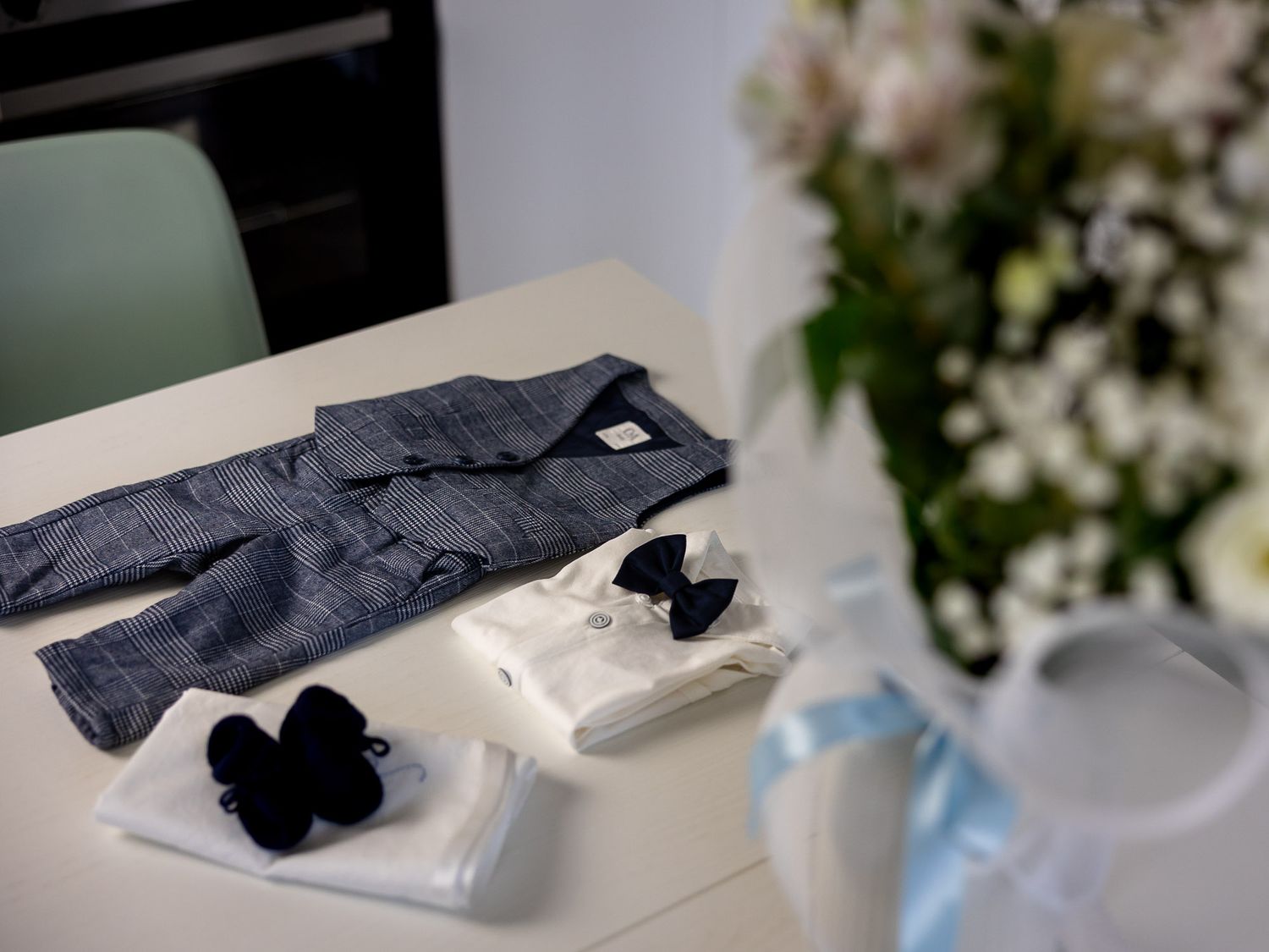Baby boy christening outfit with gray suit, white shirt, bow tie, and socks displayed on a white table.