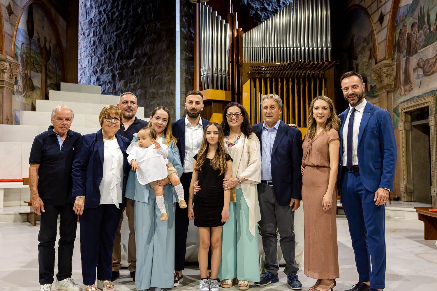 Family group portrait inside an ornate church with organ pipes, celebrating a baptism ceremony together.