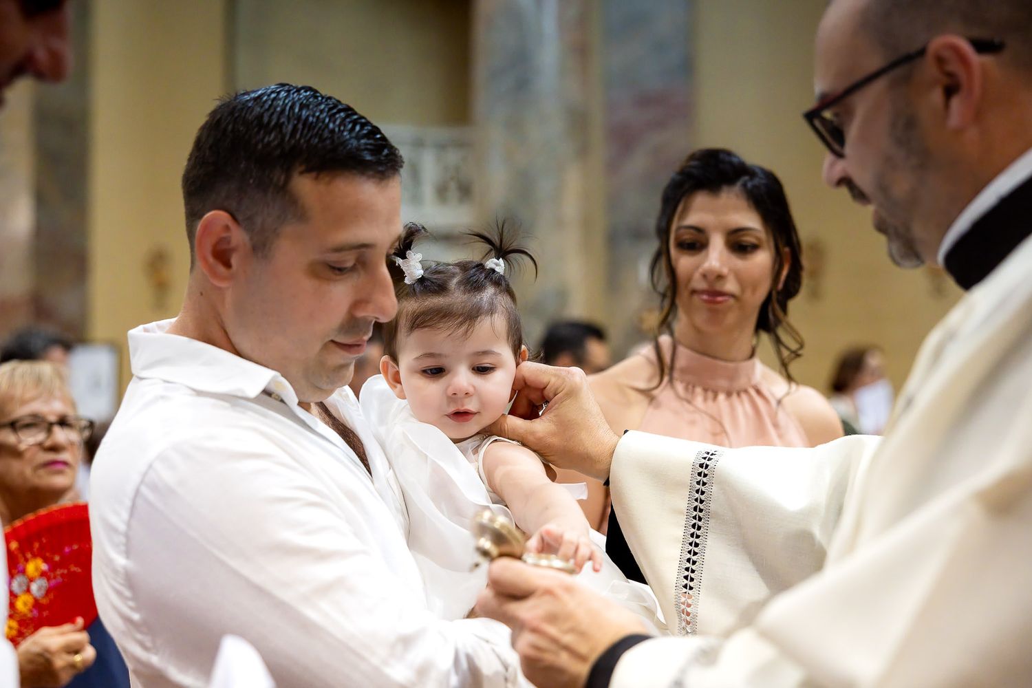 A priest baptizes a baby held by parents during a church christening ceremony.