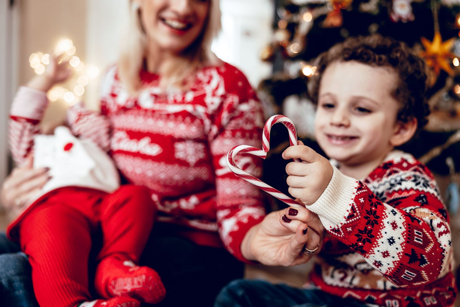 Two people wearing festive Christmas sweaters sit together opening presents during holiday celebrations.