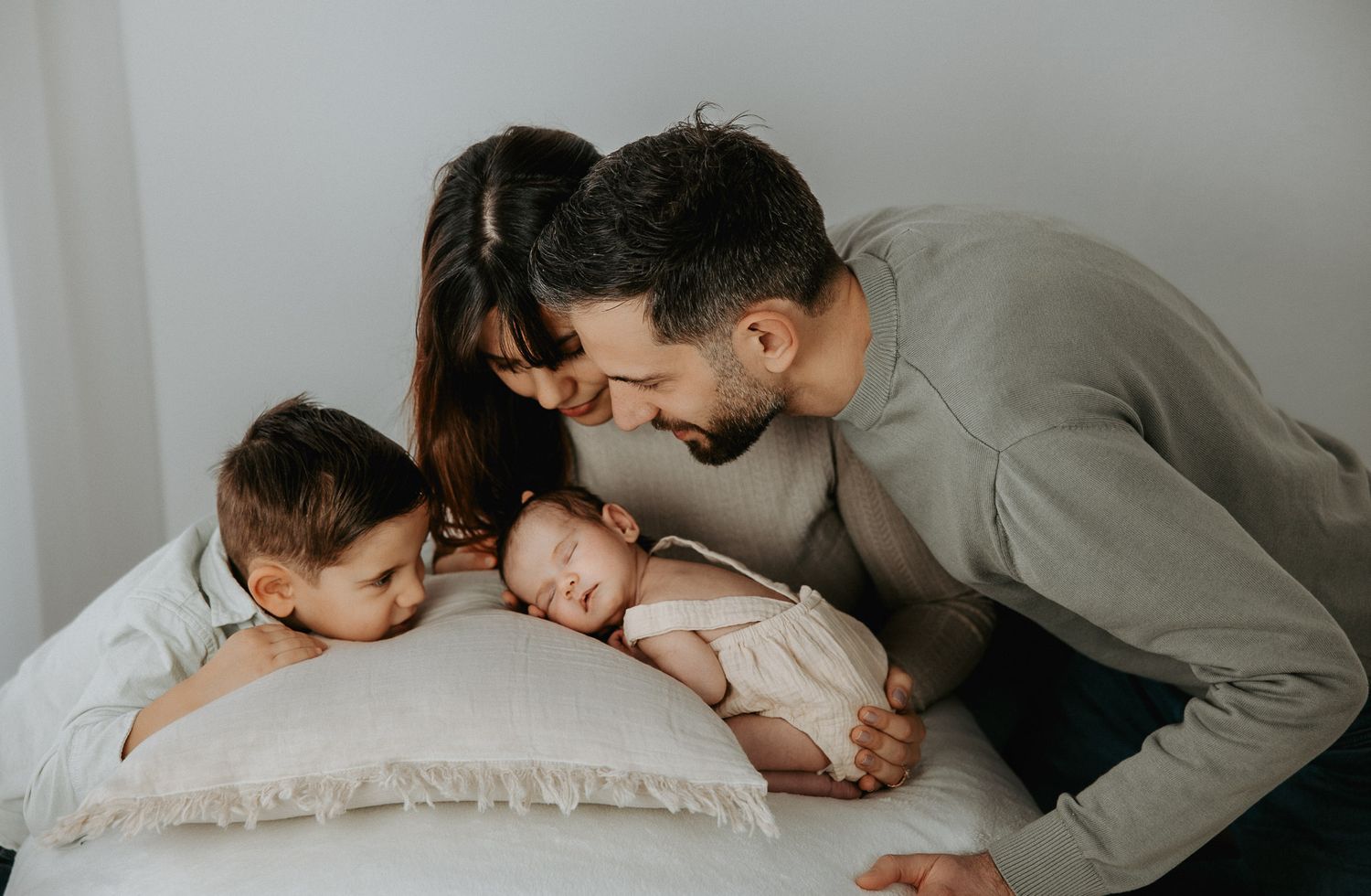 Four sequential photos show tender moments between parent and child laying together on white bedding.