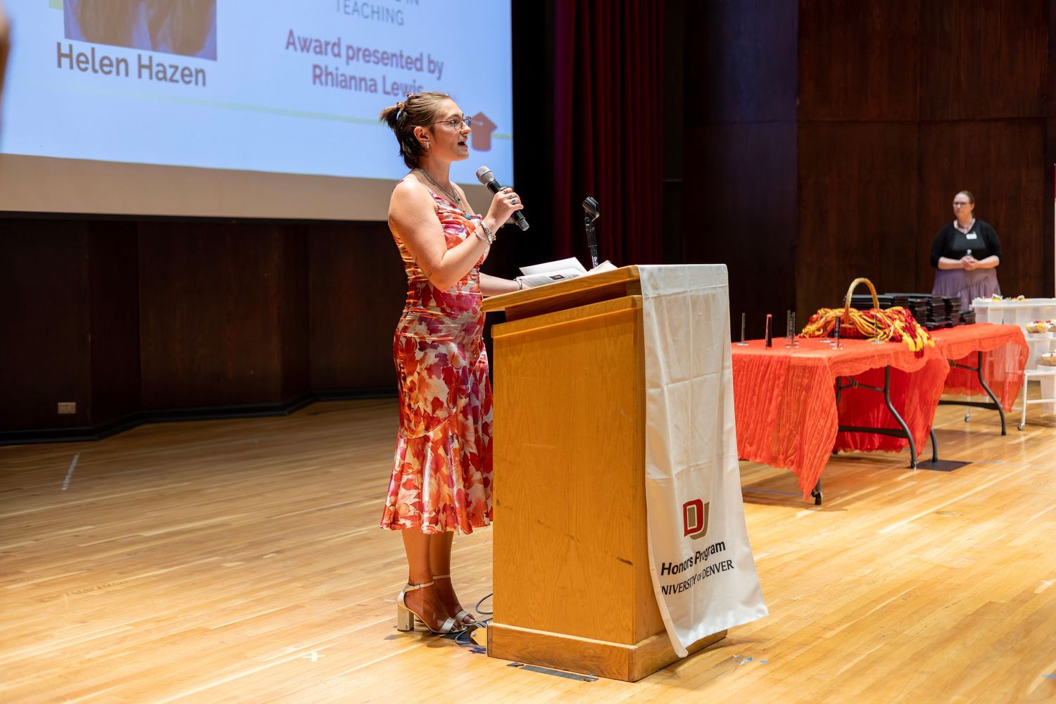 Helen Hazen accepts an award at a podium on stage during a formal ceremony in an auditorium.