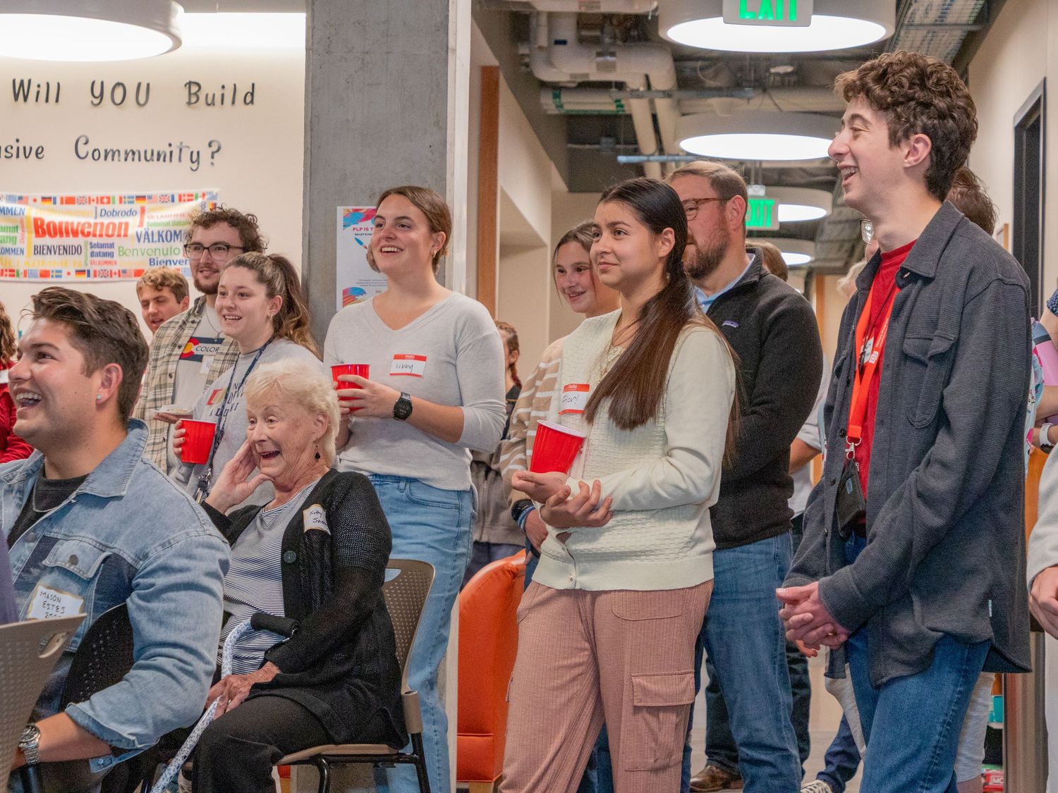 A group of students gather in a casual indoor setting, engaged in conversation and holding red cups.