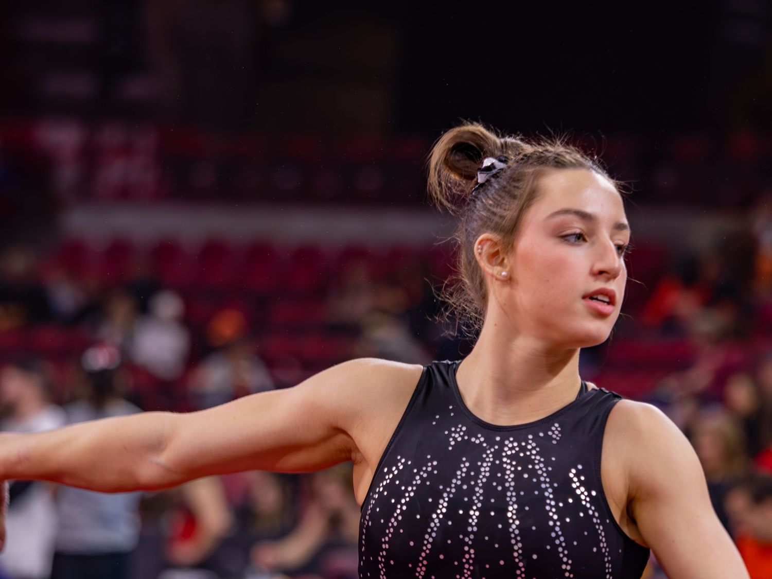 Gymnast in black sparkly leotard performs graceful floor exercise routine at competition venue.