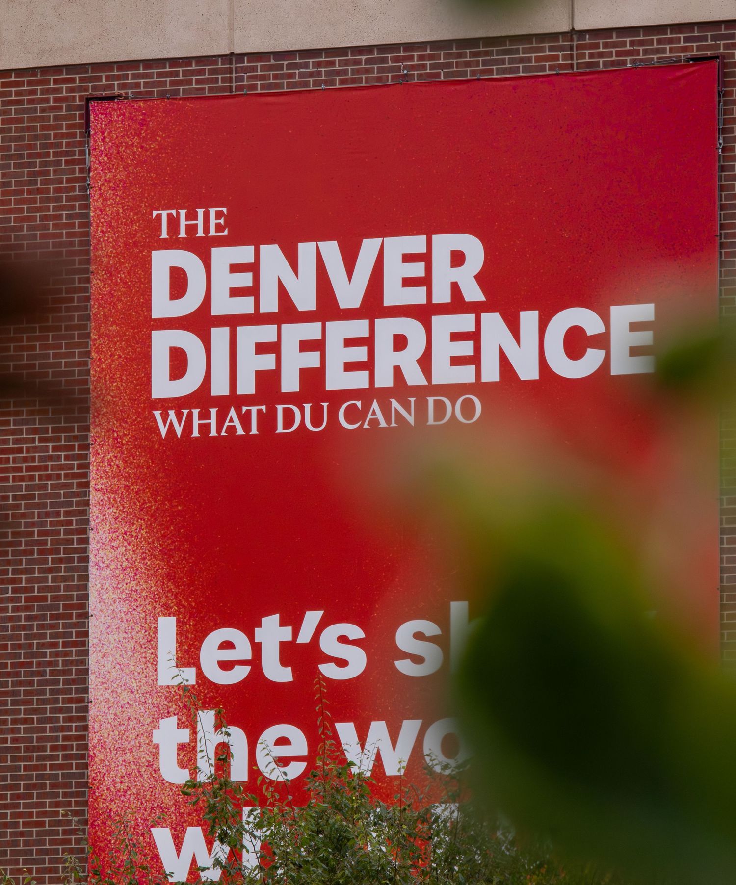 Red sign reading The Denver Difference What DU Can Do on a brick wall at University of Denver campus.