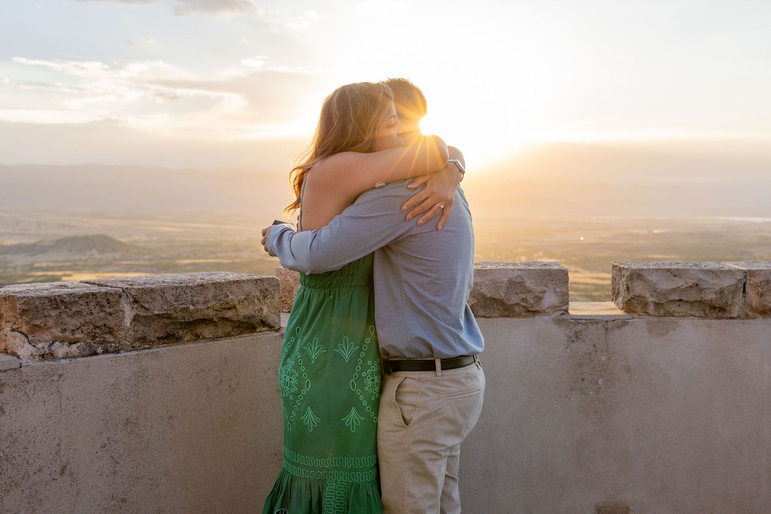 Couple embracing at sunset on a stone terrace overlooking a scenic valley landscape.