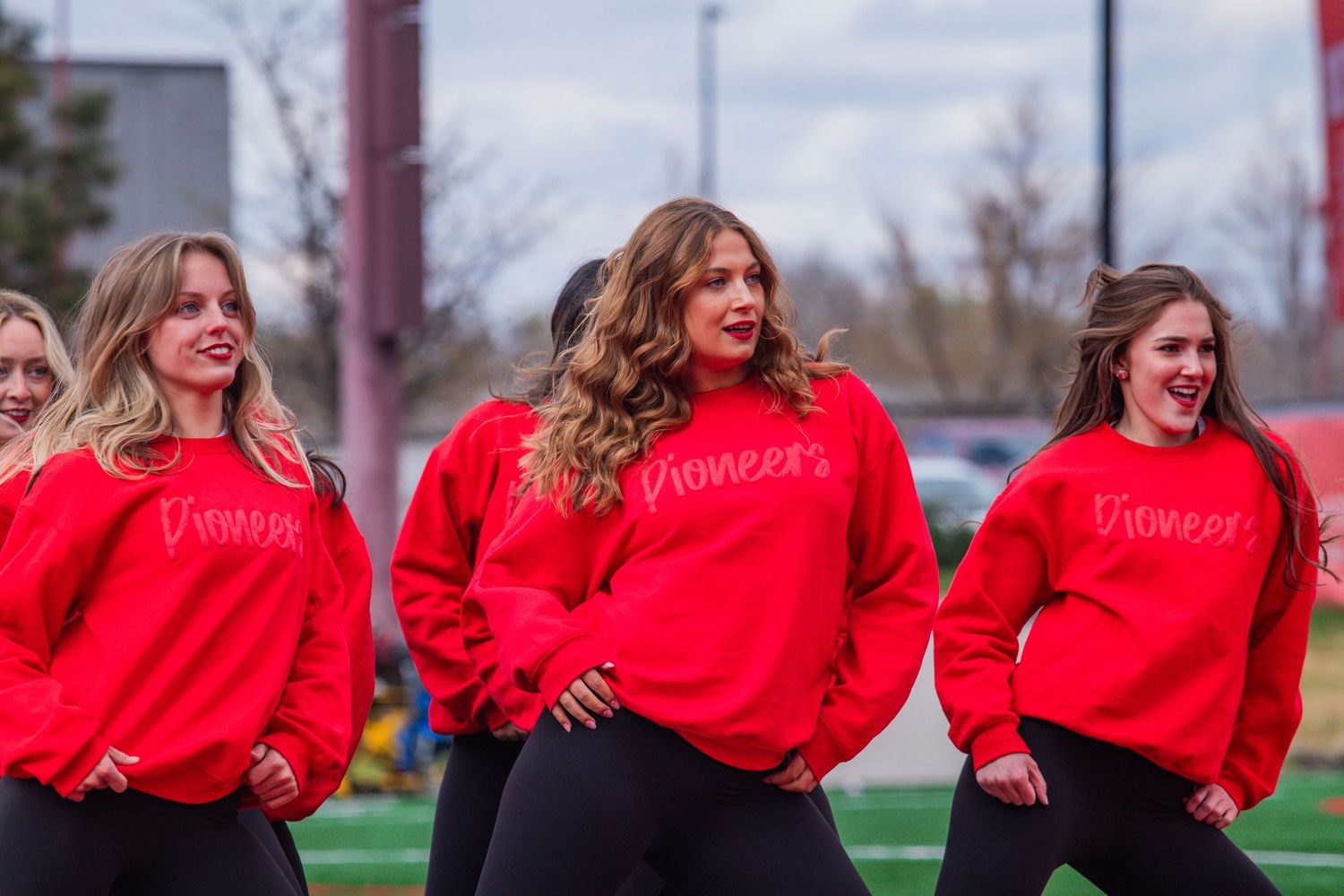 A group of women in matching bright red sweatshirts pose together outdoors on a sunny day.