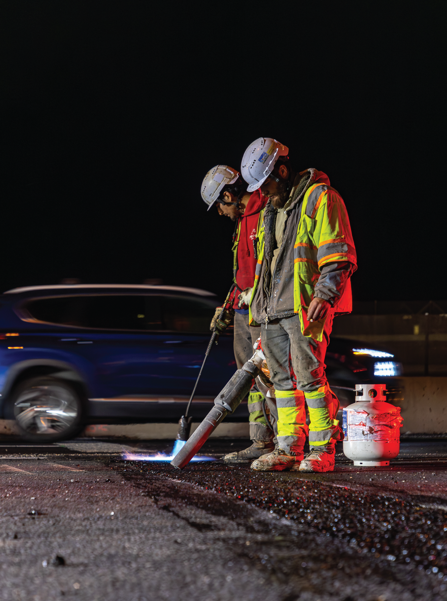 Emergency responders in reflective gear work at night on a dark road surface with scattered debris.