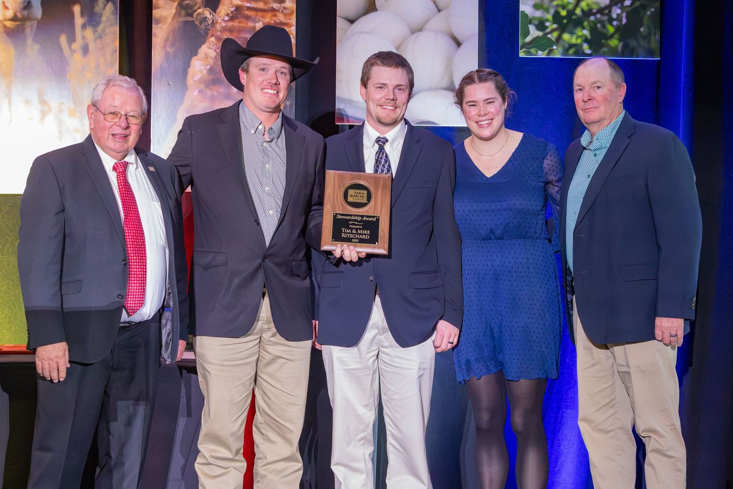 A group of people stand together at an awards ceremony or formal event against a blue backdrop.