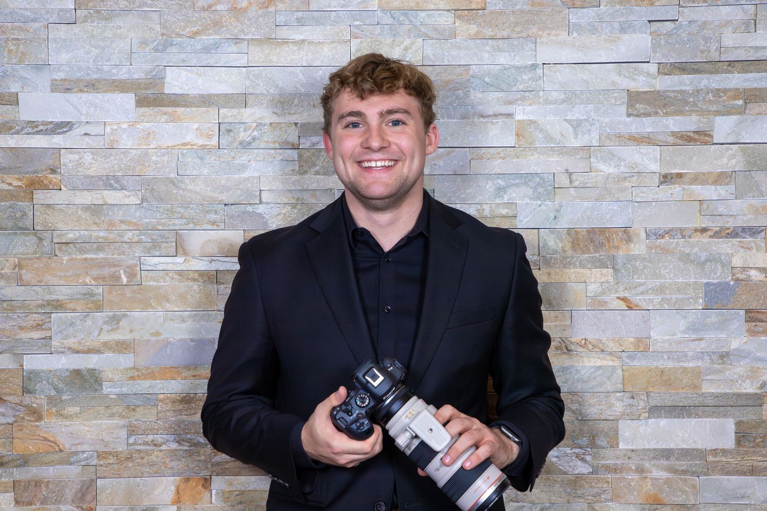 A series of four photos showing someone in a black suit jacket holding a camera against a light stone wall background.