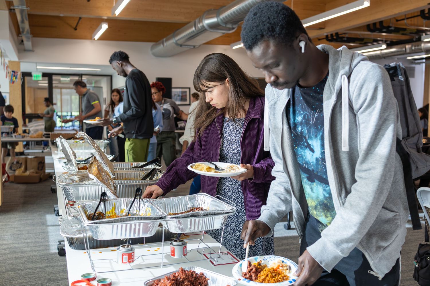 Students serving themselves at a buffet-style cafeteria food line, filling plates with various dishes.