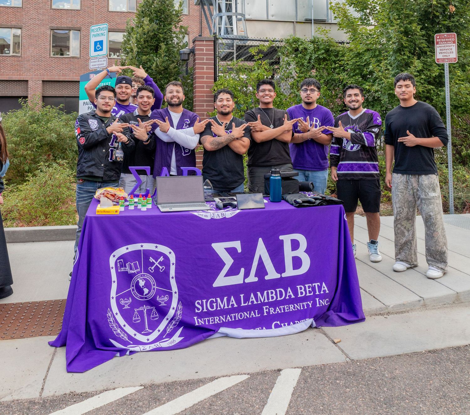 Group of students displaying purple Sigma Lambda Beta fraternity banners outdoors.