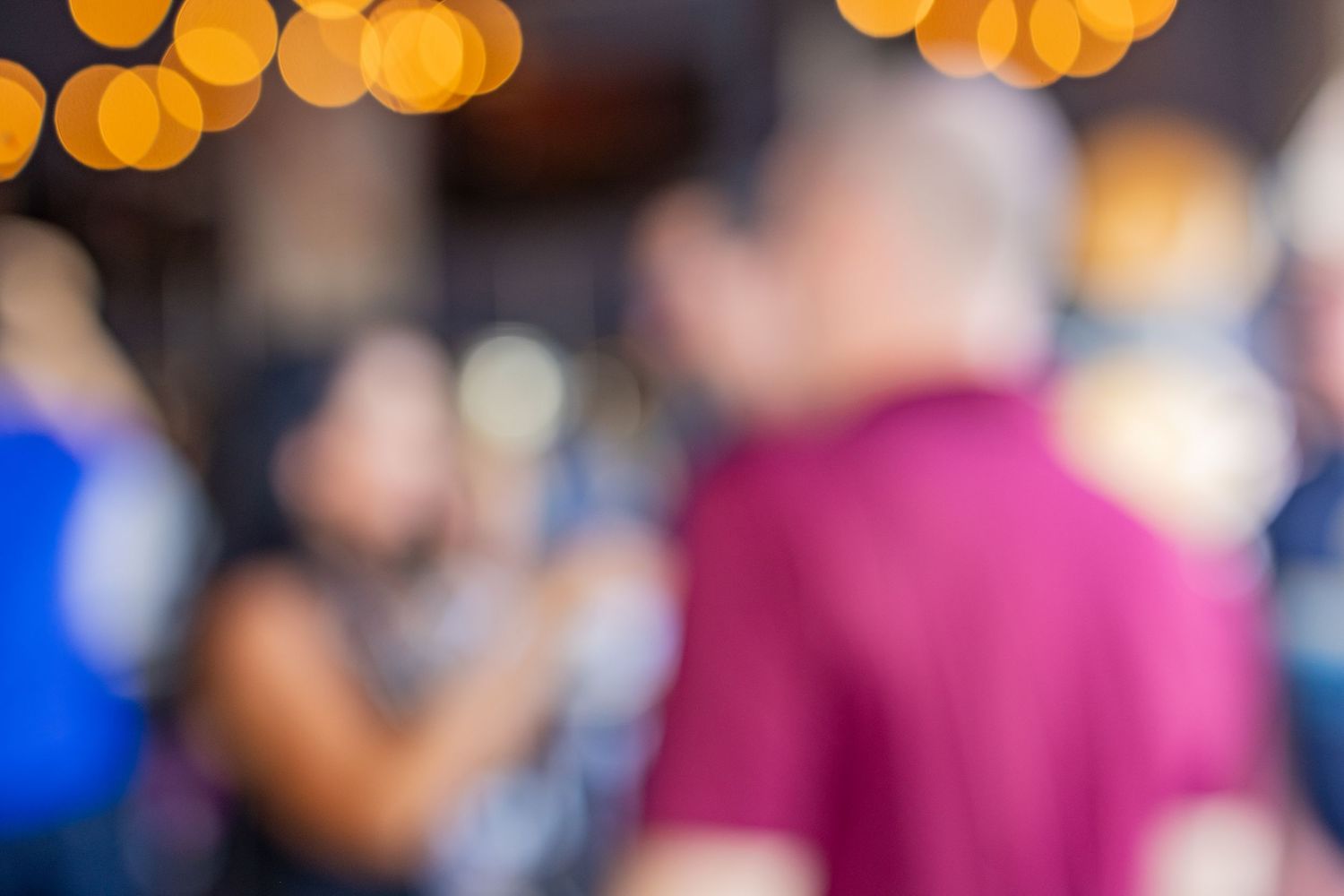 Blurred bokeh background of people socializing at a party or bar with warm golden lights overhead.