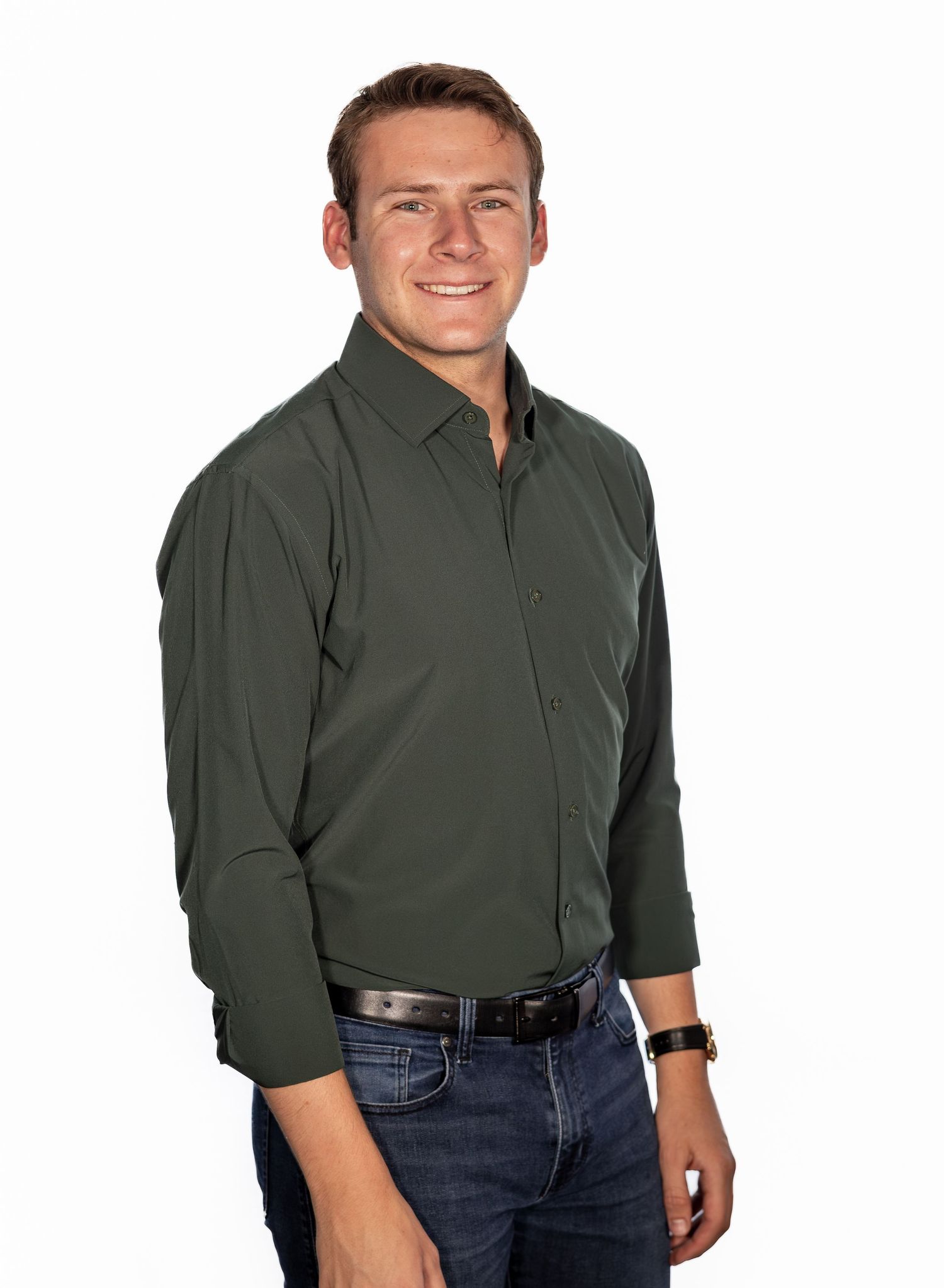 Young man smiling in dark green button-up shirt and jeans, posing against white background.