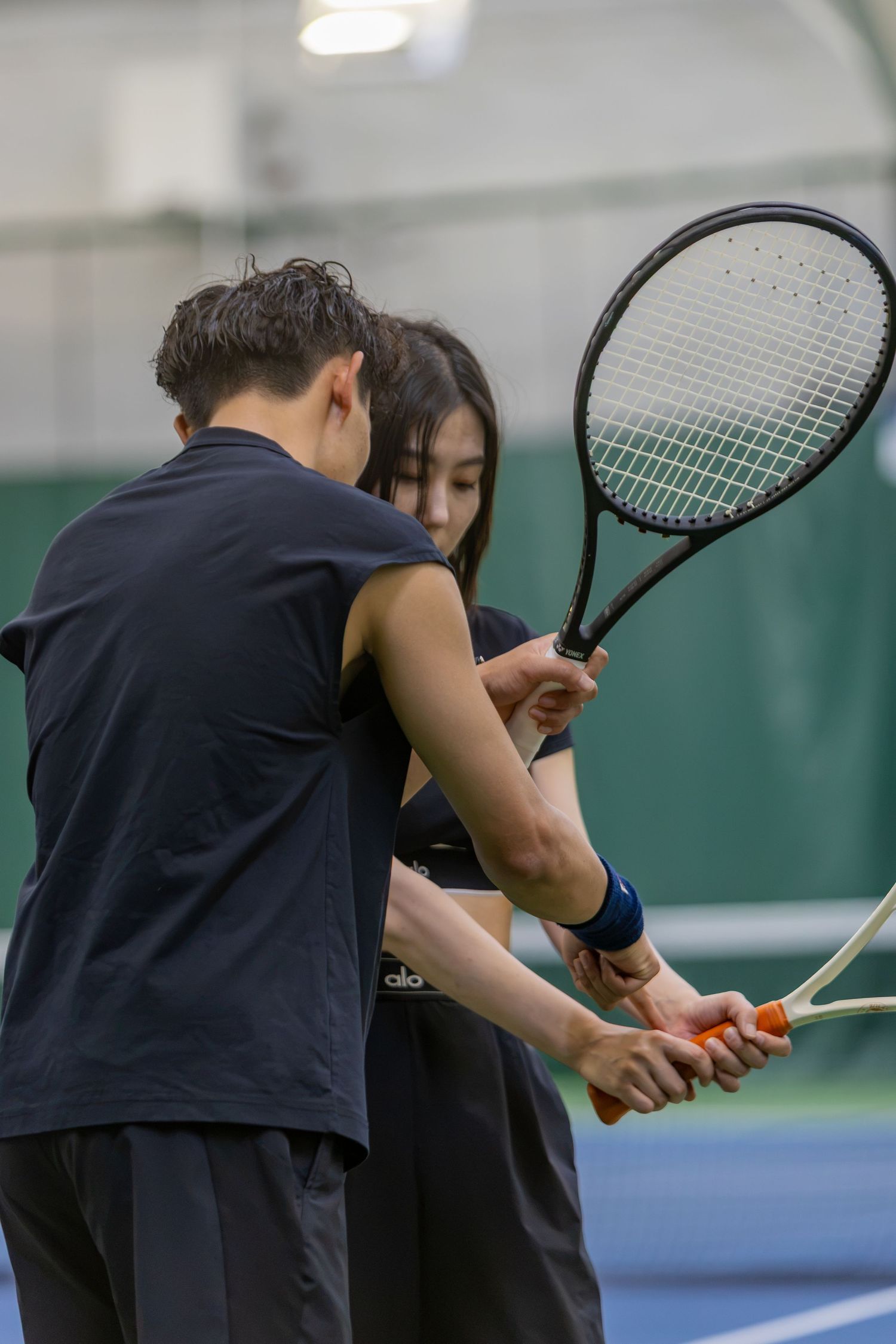 Tennis coach guiding a young woman on proper racket grip technique on an indoor tennis court.