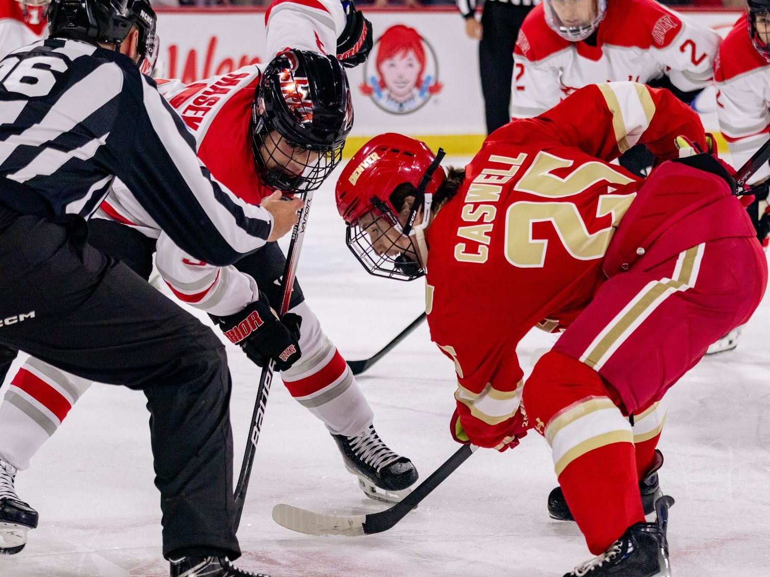 Ice hockey players in red and black jerseys battle for the puck during an intense game.