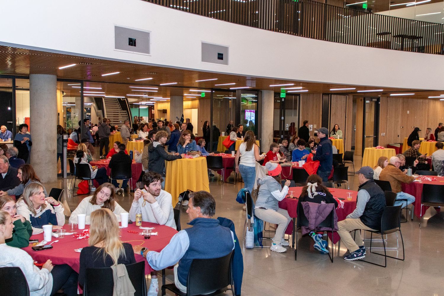 Students and faculty gather at round tables in a modern university atrium during a campus dining or networking event.