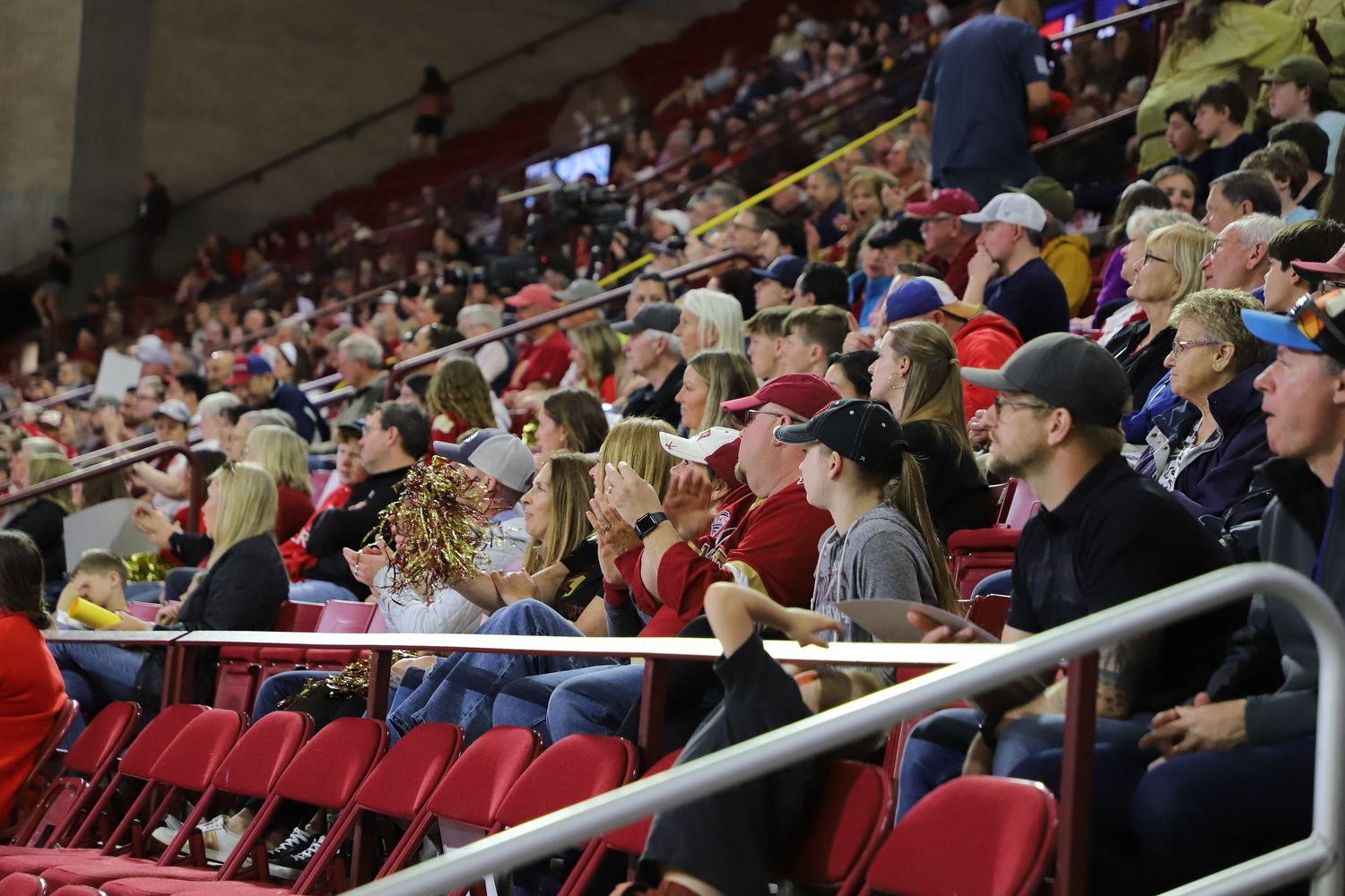 Crowd of fans sitting in red stadium seats watching a live sporting event in a large indoor arena.