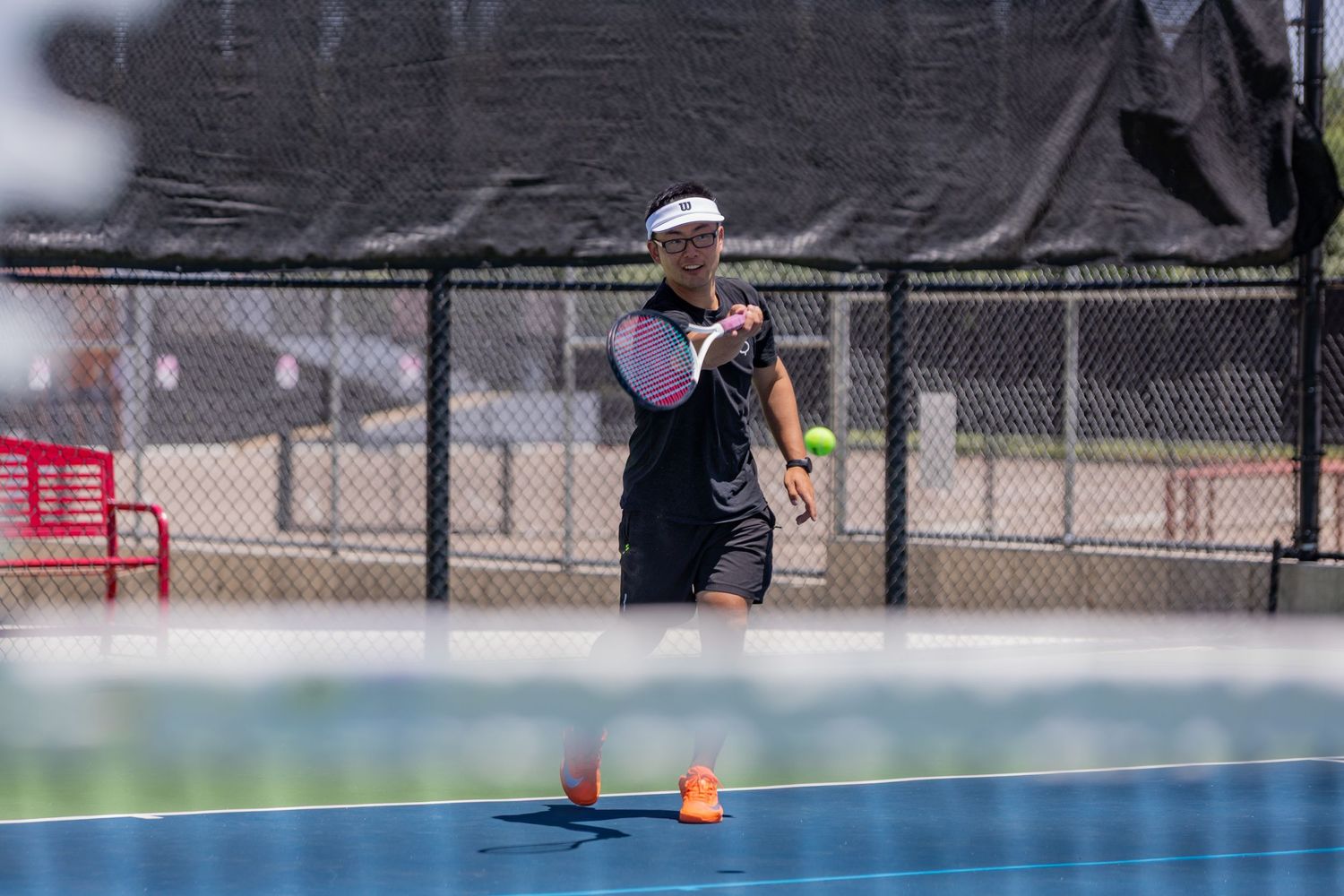 Tennis player in black and pink outfit preparing to hit a shot on a blue outdoor court.