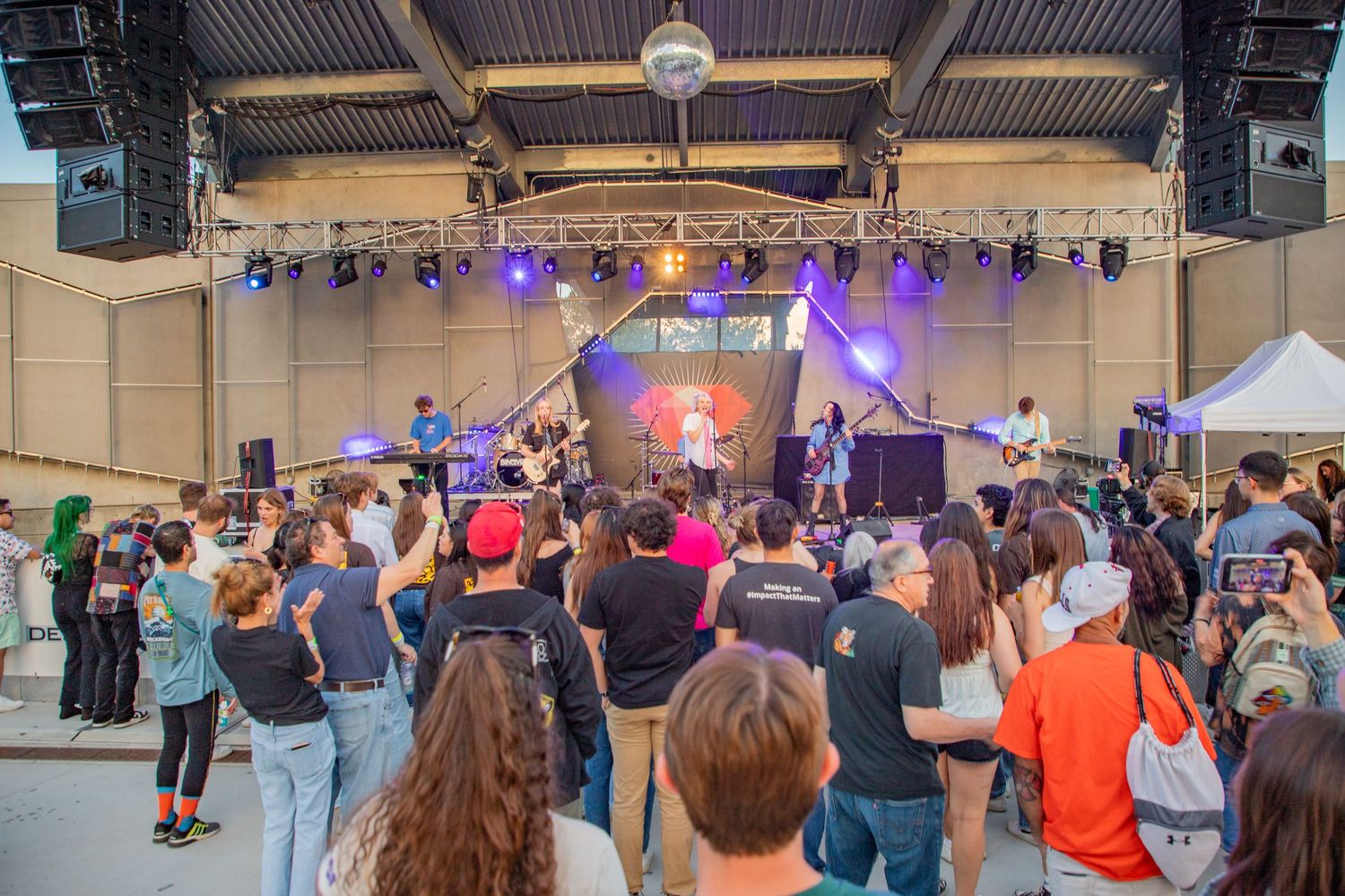 Crowd enjoying a live outdoor concert on a stage with colorful lights and a disco ball at a music festival.