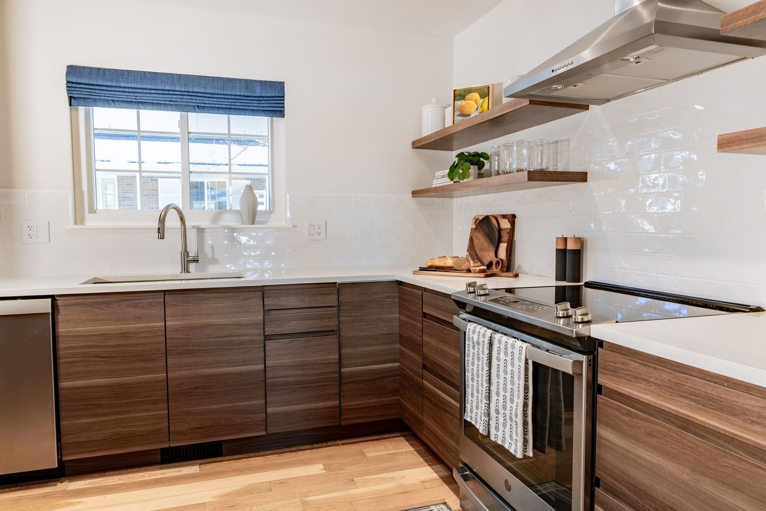 Modern kitchen design featuring dark wood cabinets, white countertops, and floating wood shelves against a white backsplash.
