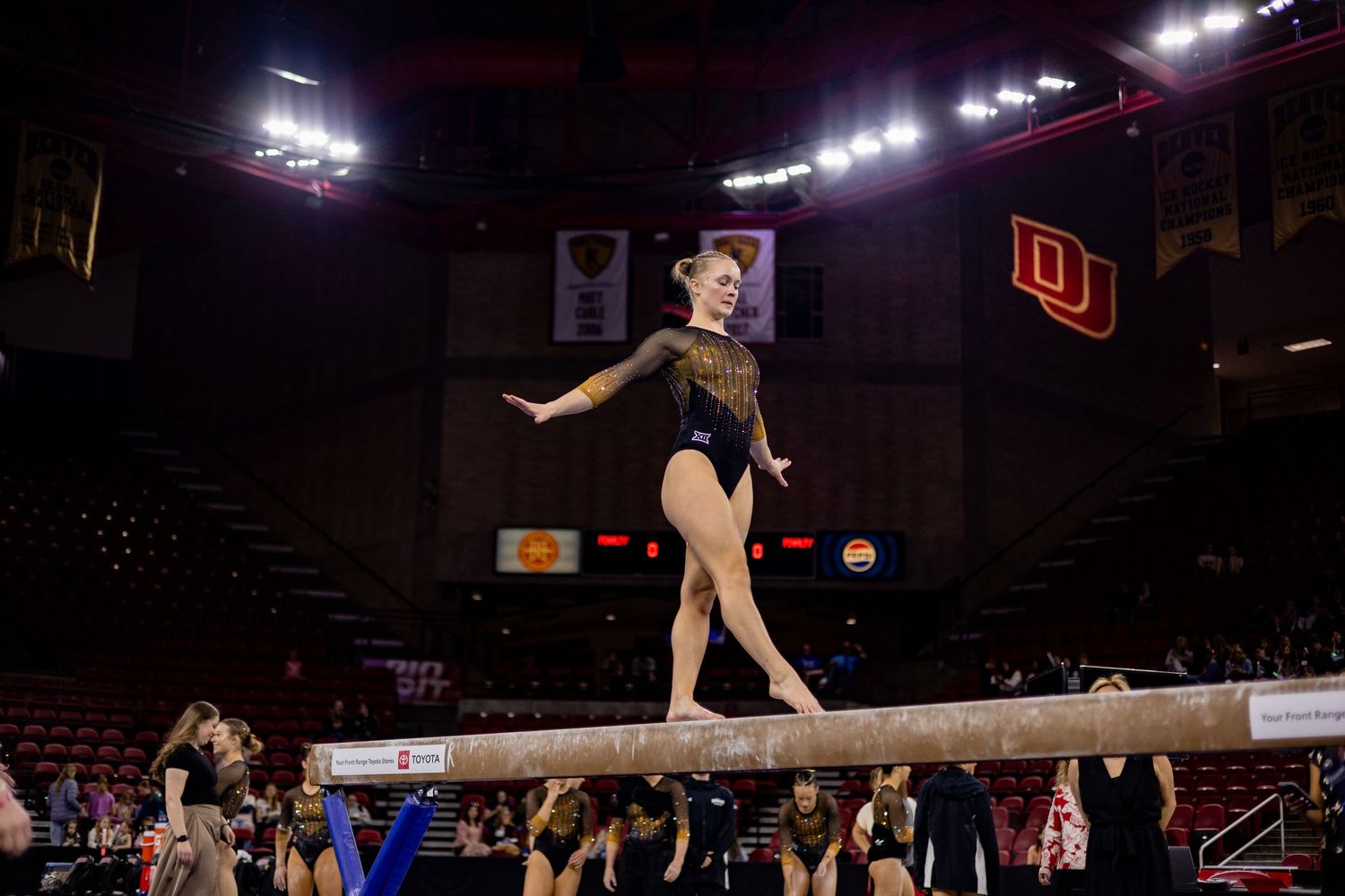 Gymnast performs graceful routine on balance beam during competition at arena with spotlights illuminating the stage.