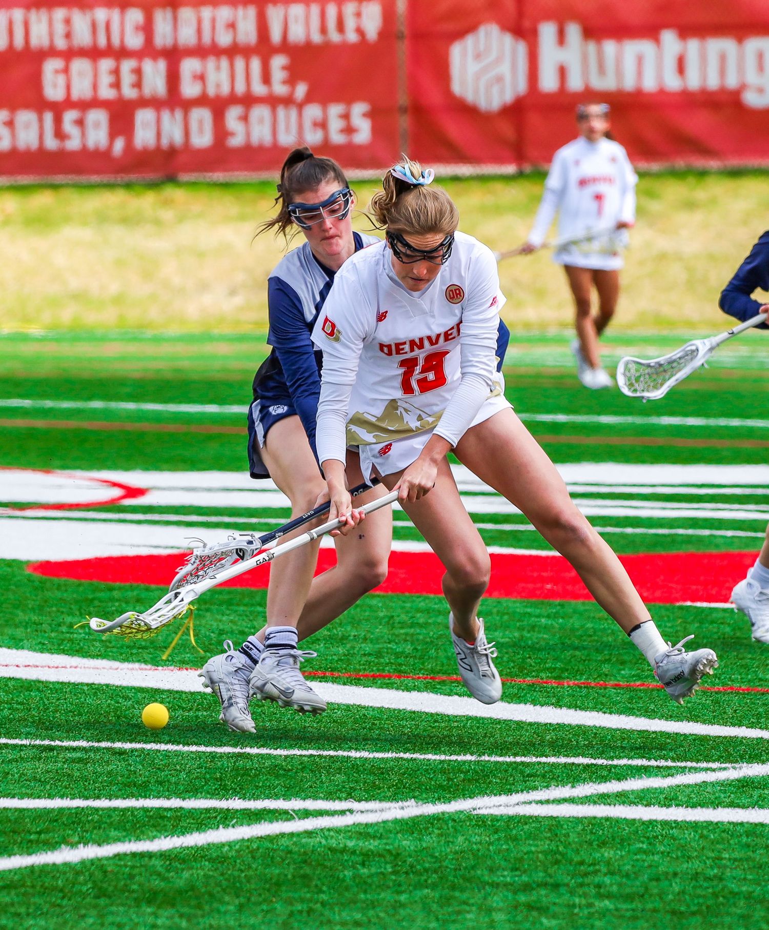 Players dive for loose balls during an intense lacrosse practice drill on artificial turf.