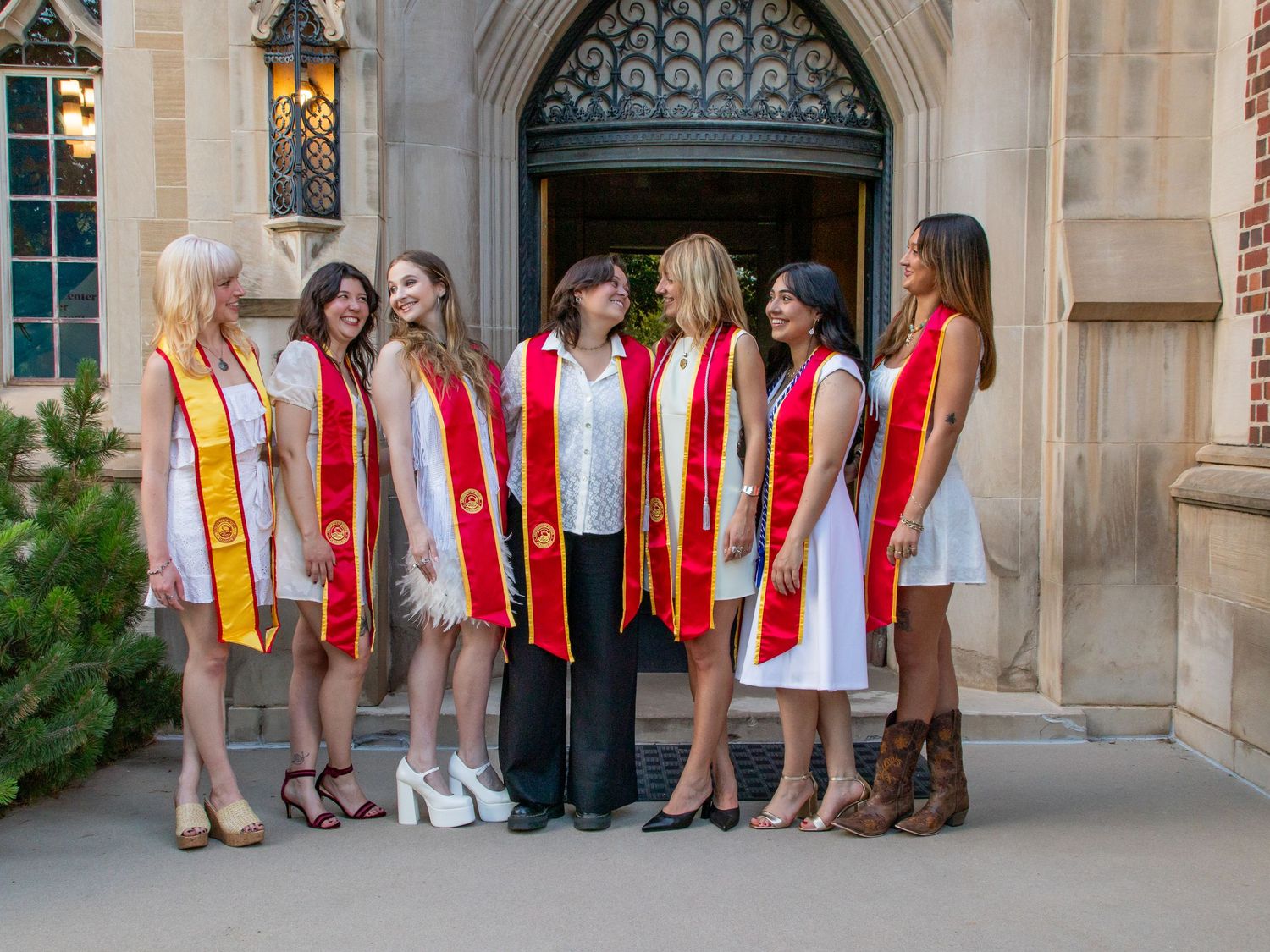 Group of graduates in red stoles pose together in front of ornate archway.
