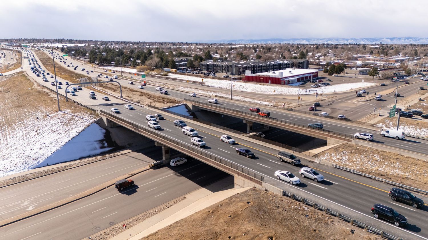 Panoramic aerial view of a highway intersection with multiple lanes and traffic in an urban setting during daytime.