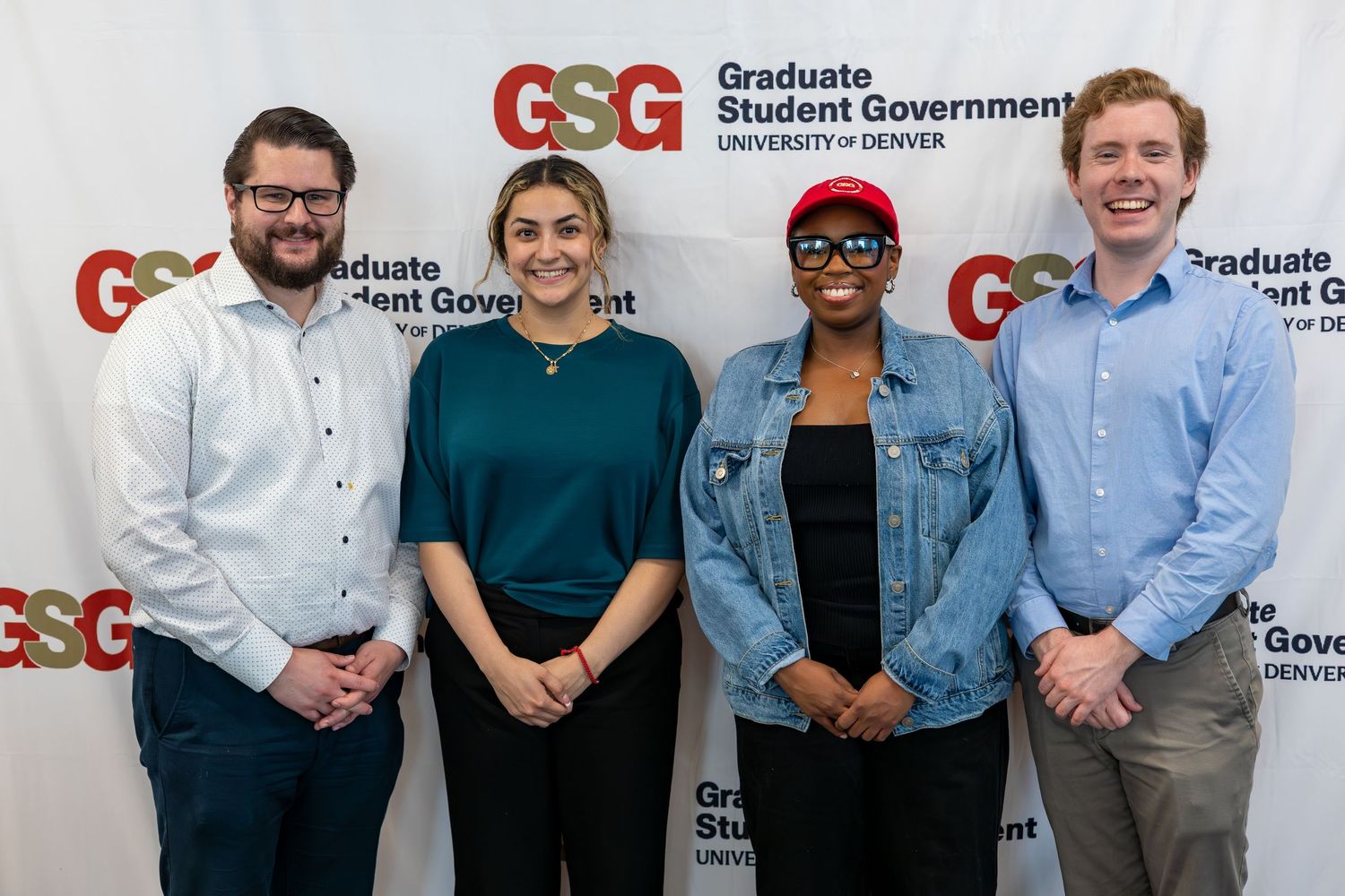 Four graduate students smile together in front of a Graduate Student Government University of Denver branded backdrop.