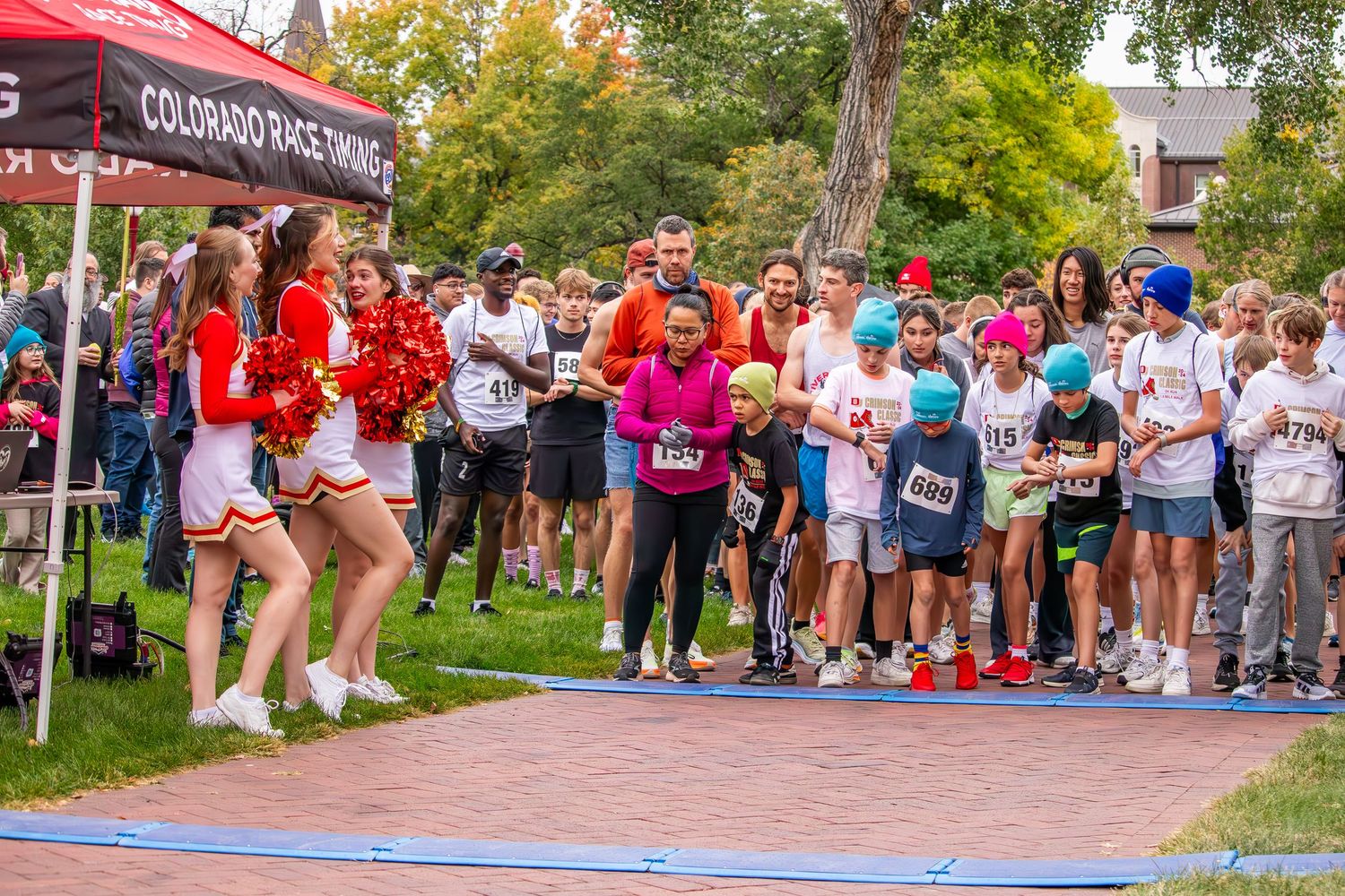 Cheerleaders and runners gather at the start line of a Colorado Race Timing outdoor 5K charity run event.