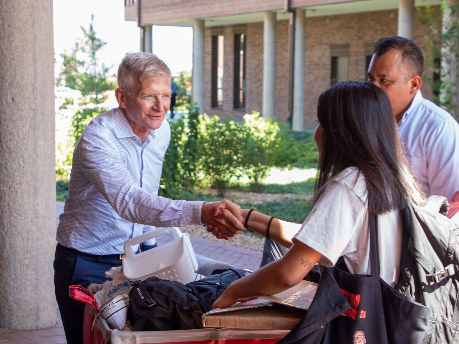 A group of people in business attire shake hands and interact during a networking event in an outdoor setting.