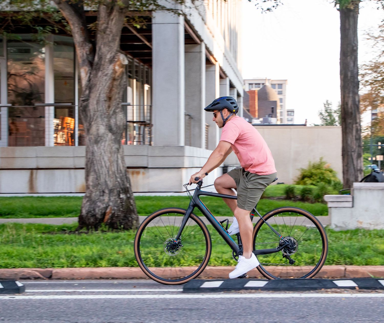 A cyclist in pink rides a road bike along a tree-lined residential street on a sunny day.