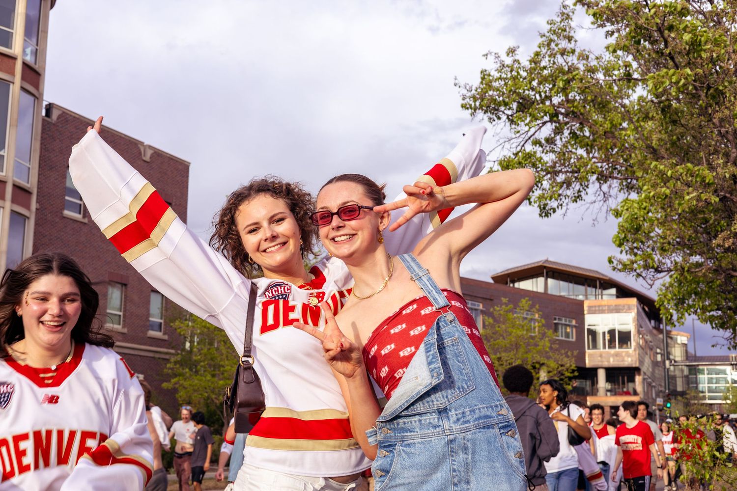 Two smiling University of Denver fans pose outdoors in school spirit attire during a campus event.