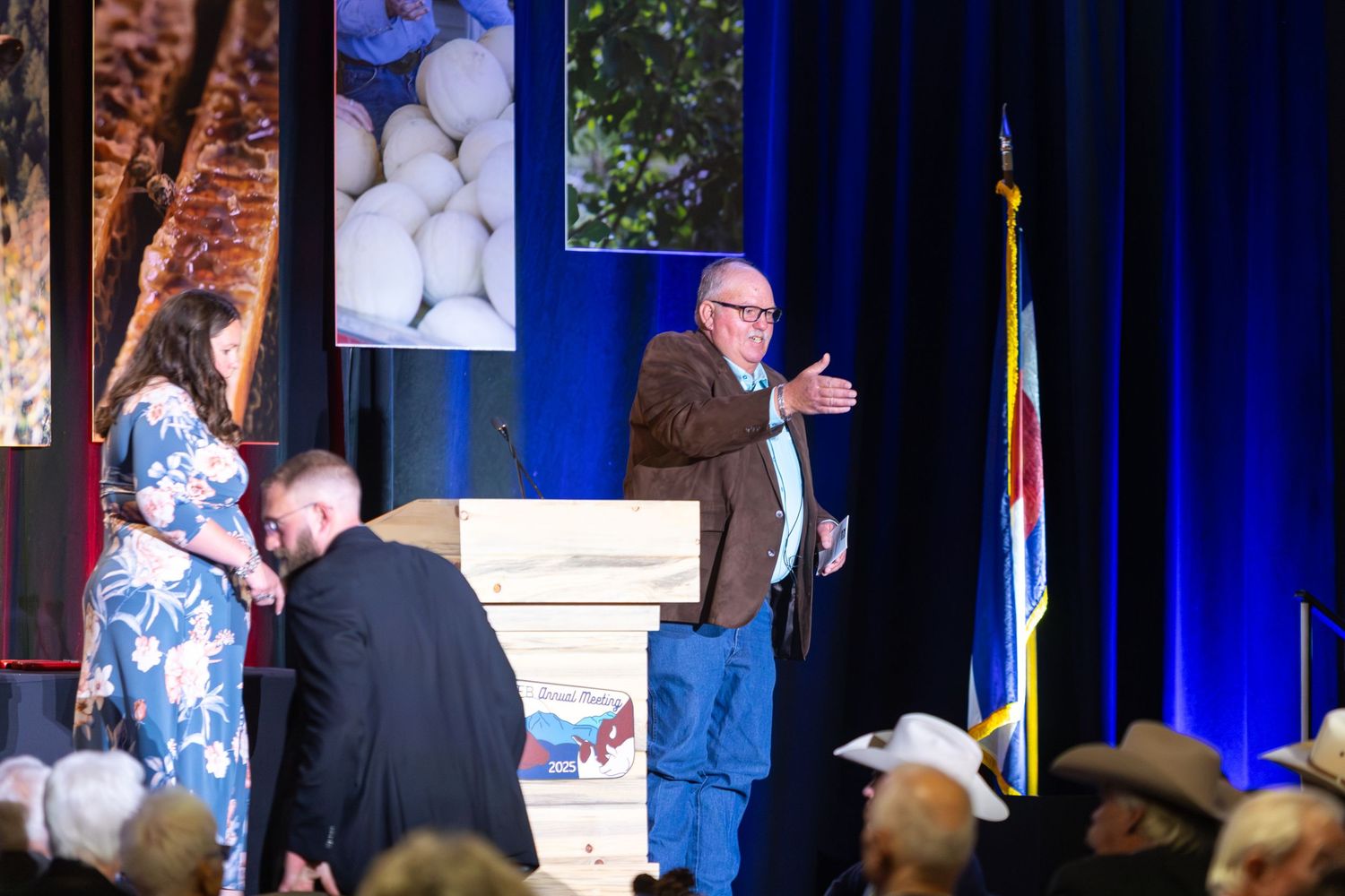 A series of speakers and presenters on stage at a conference or event with blue lighting and backdrop.