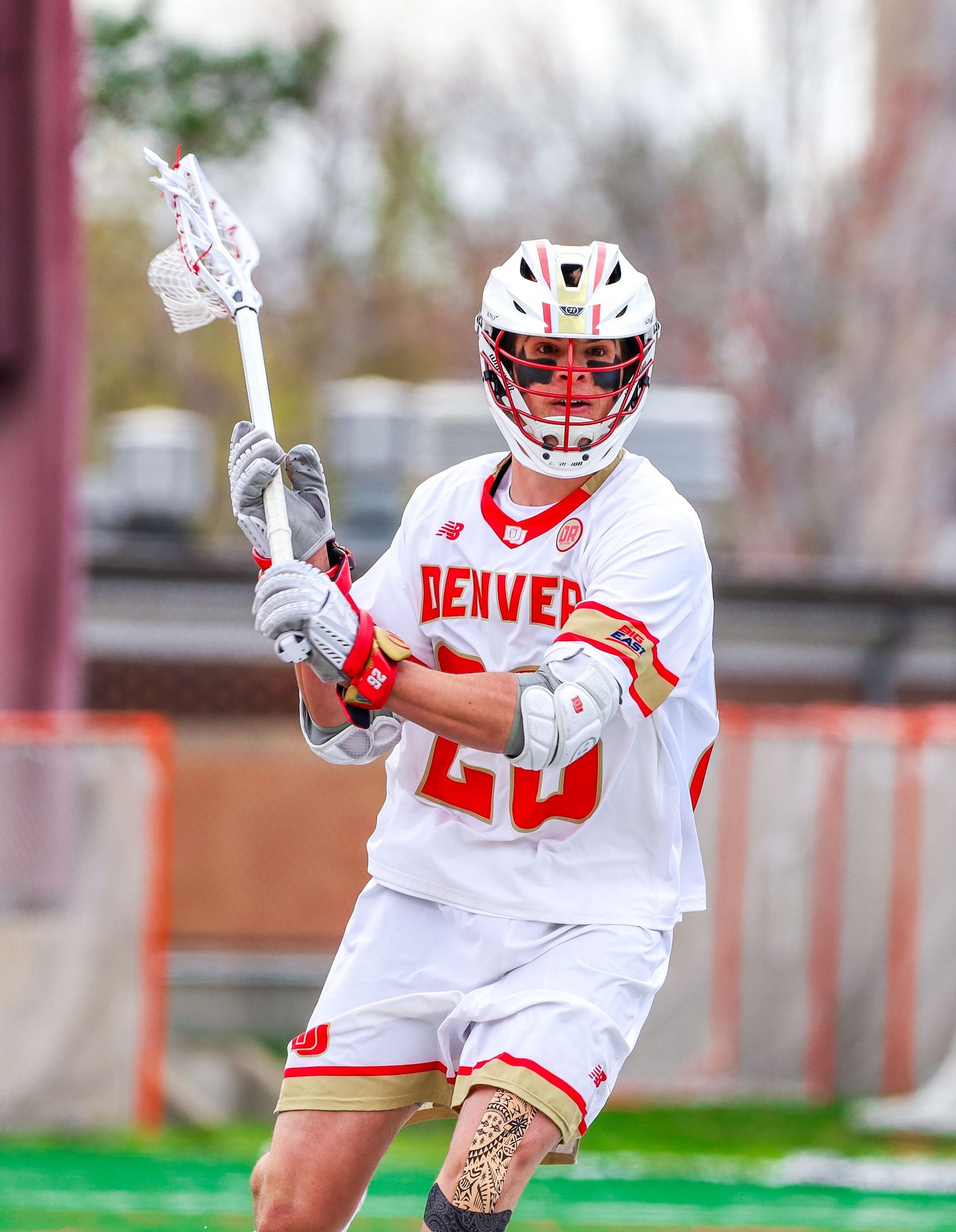 Denver lacrosse players in white uniforms practice offensive maneuvers on the field.