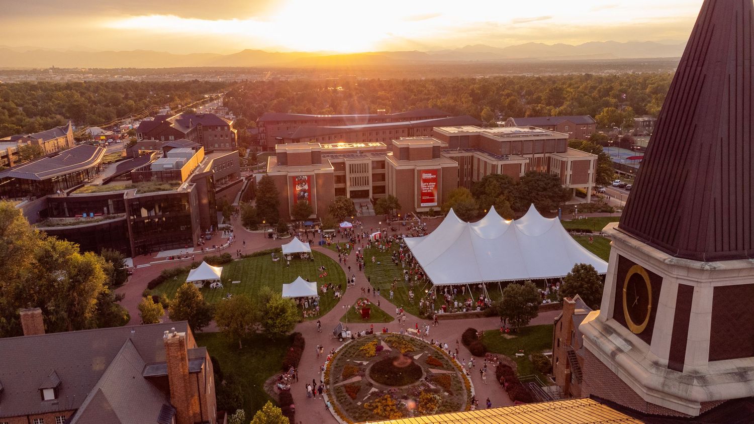 Aerial sunset view of a vibrant outdoor event on a university campus with a large white tent and lush greenery.