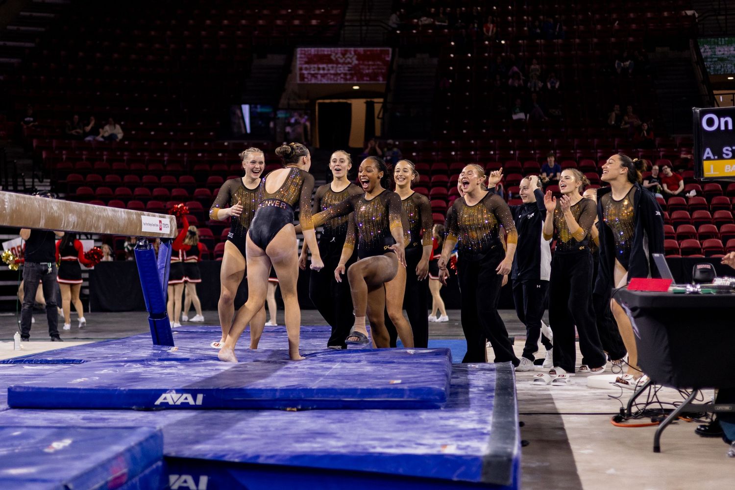 Gymnasts practice routines on blue mats during a competition event in a large indoor arena.