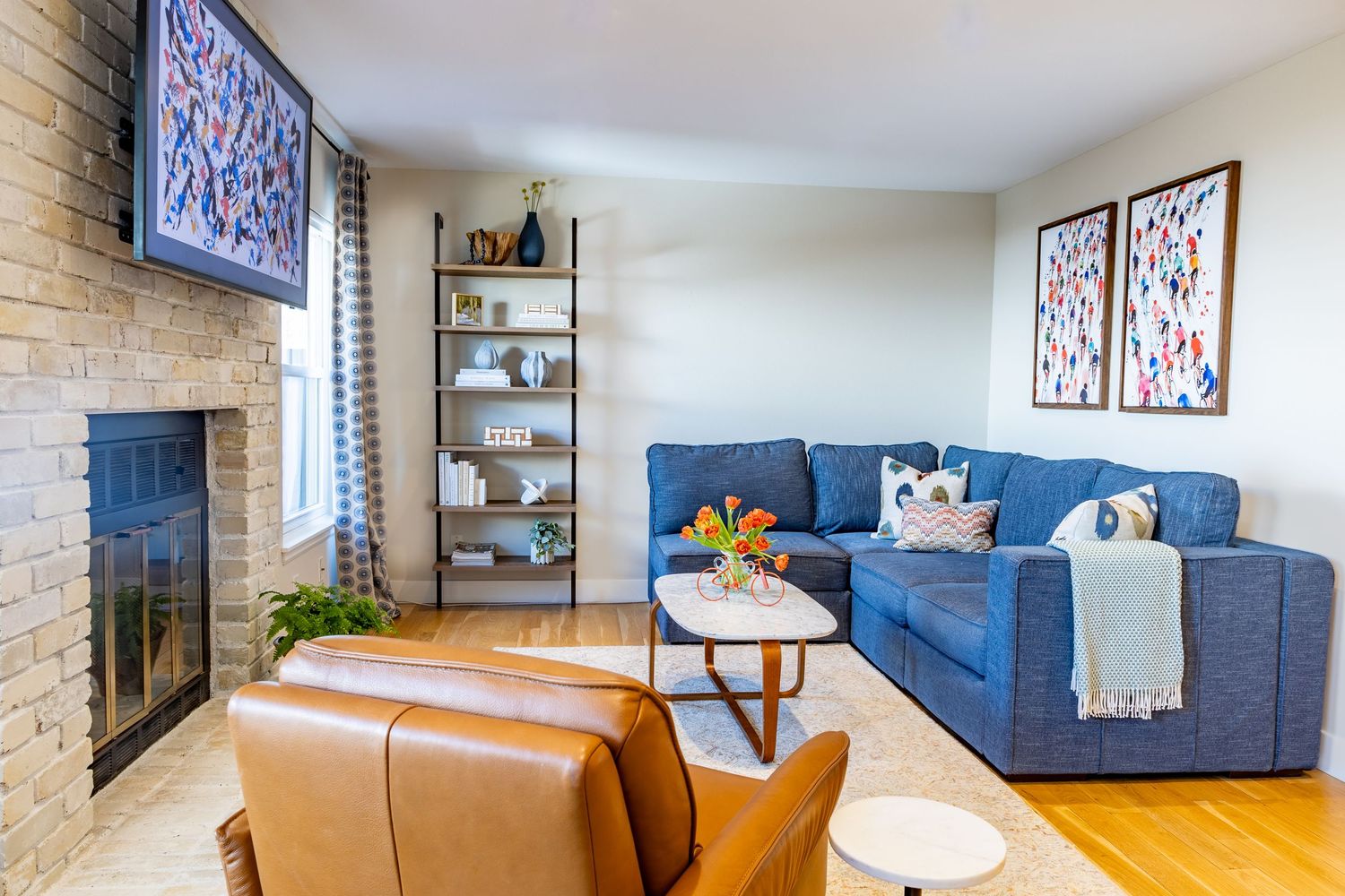 Modern living room interior with blue sofa, tan leather couch, and exposed brick wall featuring minimalist decor.