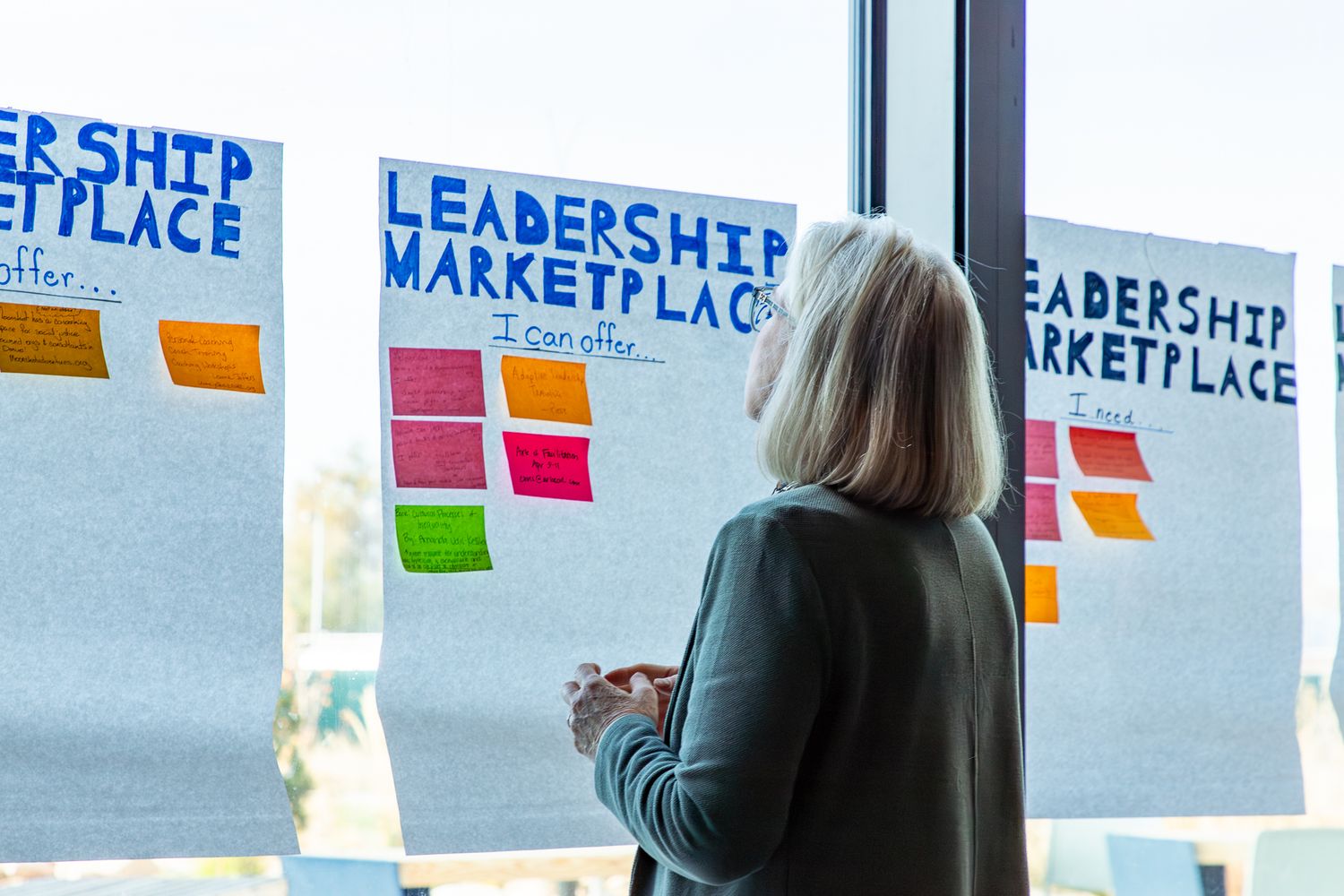Someone looks at colorful sticky notes on a window with Leadership Marketplace text displayed above.