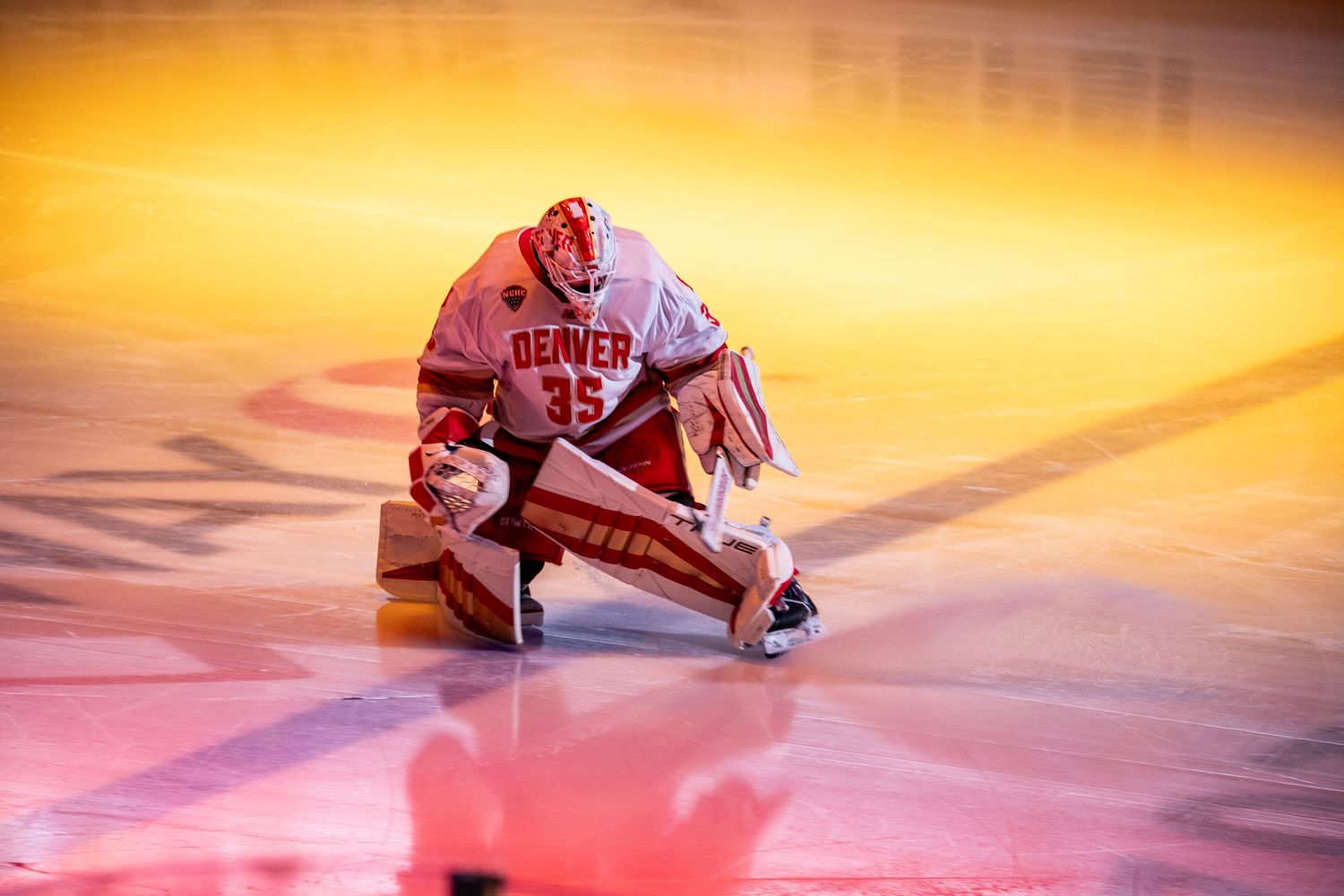 Hockey players glide on ice rink under dramatic orange lighting during pre-game ceremony.
