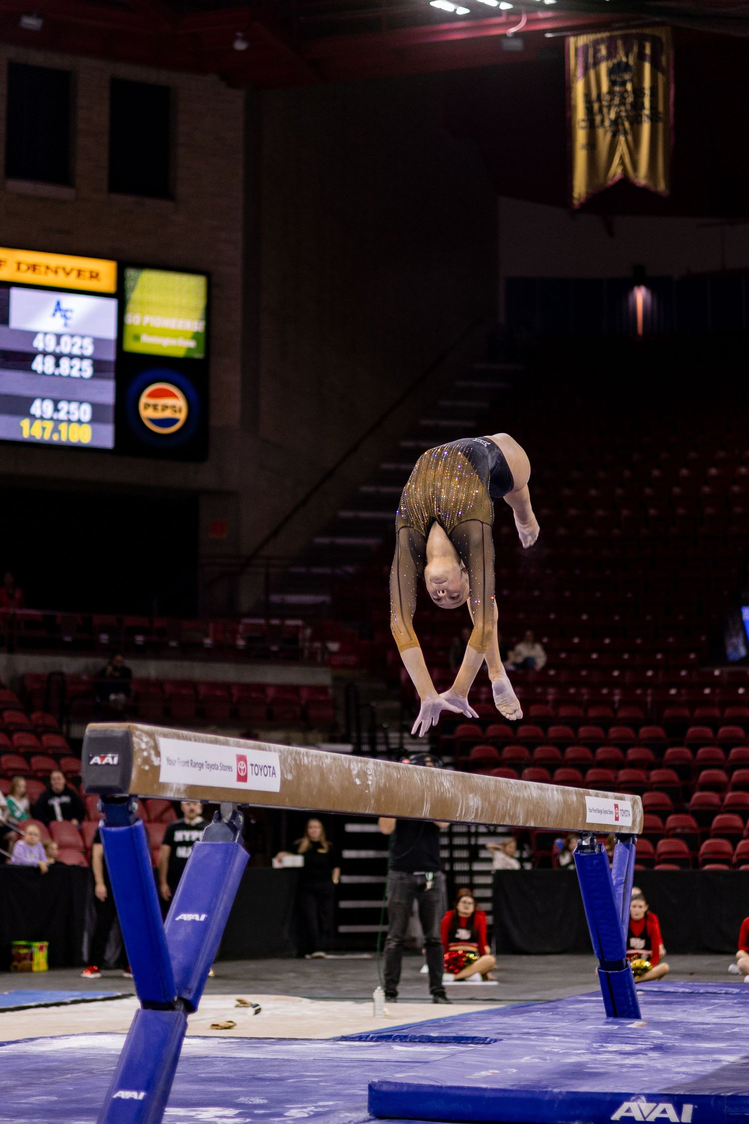 A gymnast performs a back flip sequence on the balance beam during a competition in an indoor arena.