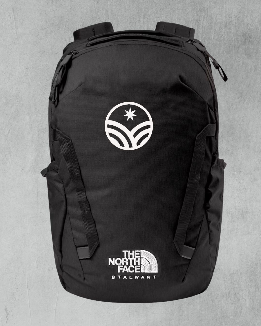 Black The North Face Stalwart backpack with white logo on grey background.