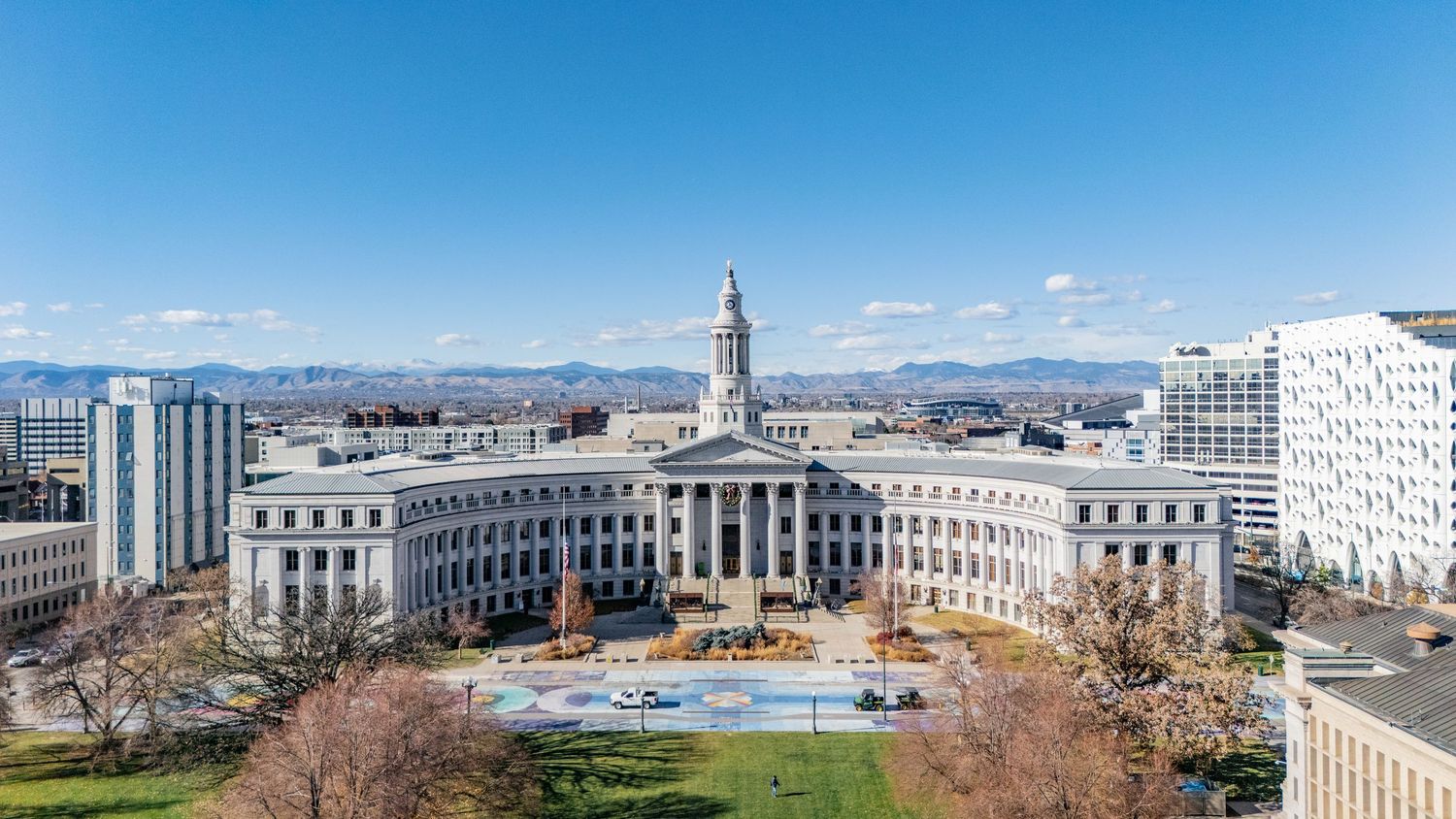 Aerial panoramic view of Denver City and County Building with snow-capped mountains in the background on a sunny day.